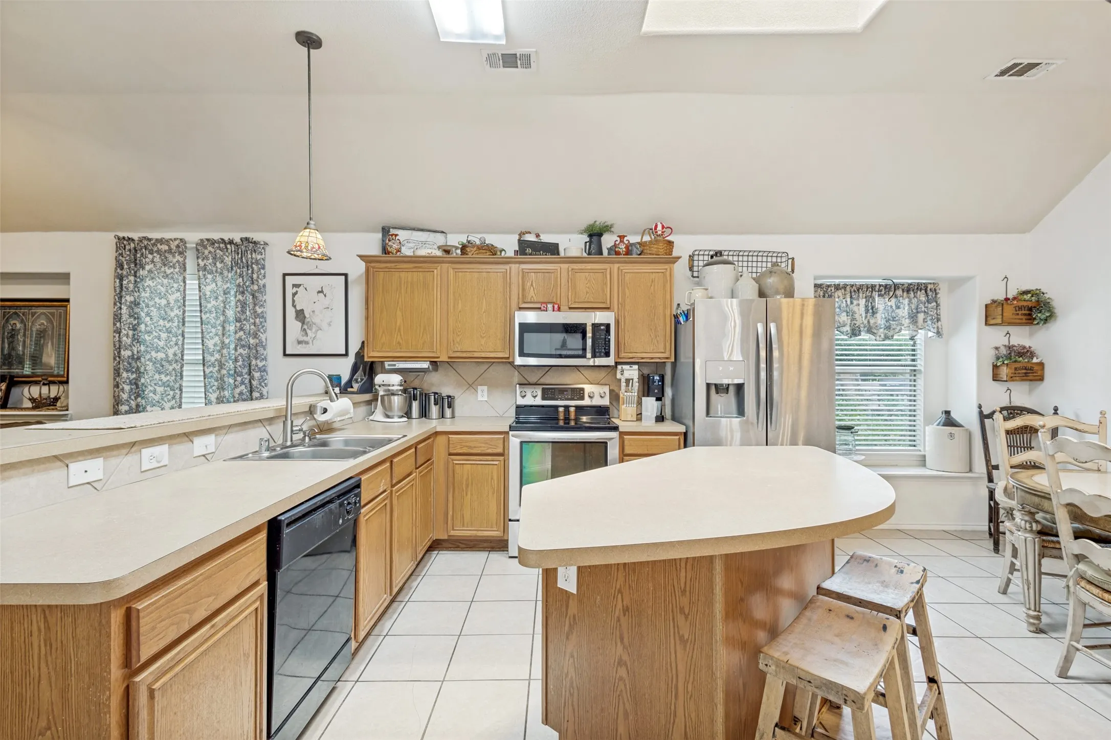 Kitchen featuring wood cabinetry, stainless steel appliances, a center island, and white tile flooring