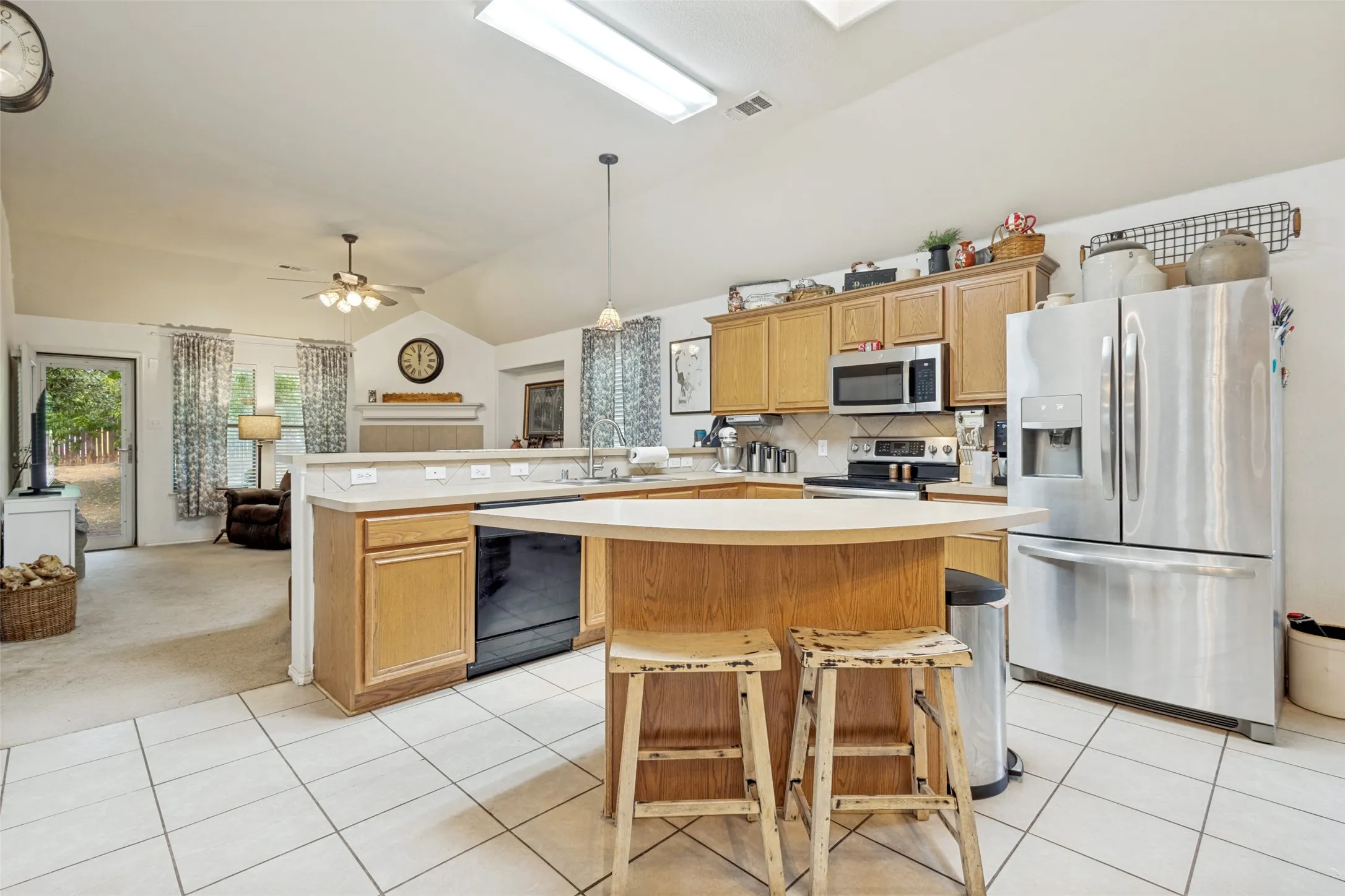Kitchen featuring tile flooring, wood-finish cabinetry, stainless steel appliances, and a breakfast bar
