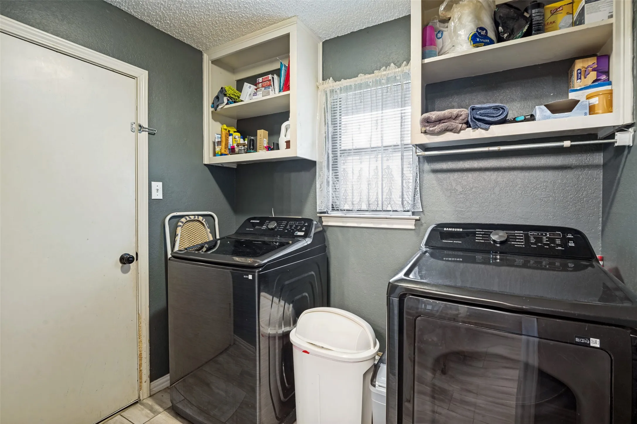 Utility area featuring built-in shelving, a window with blinds, and tiled flooring