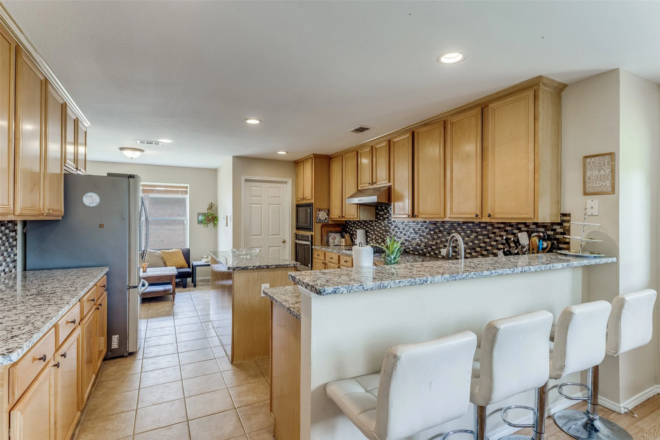 Kitchen featuring light wood cabinetry, granite-finish countertops, tile flooring, and a mosaic tile backsplash