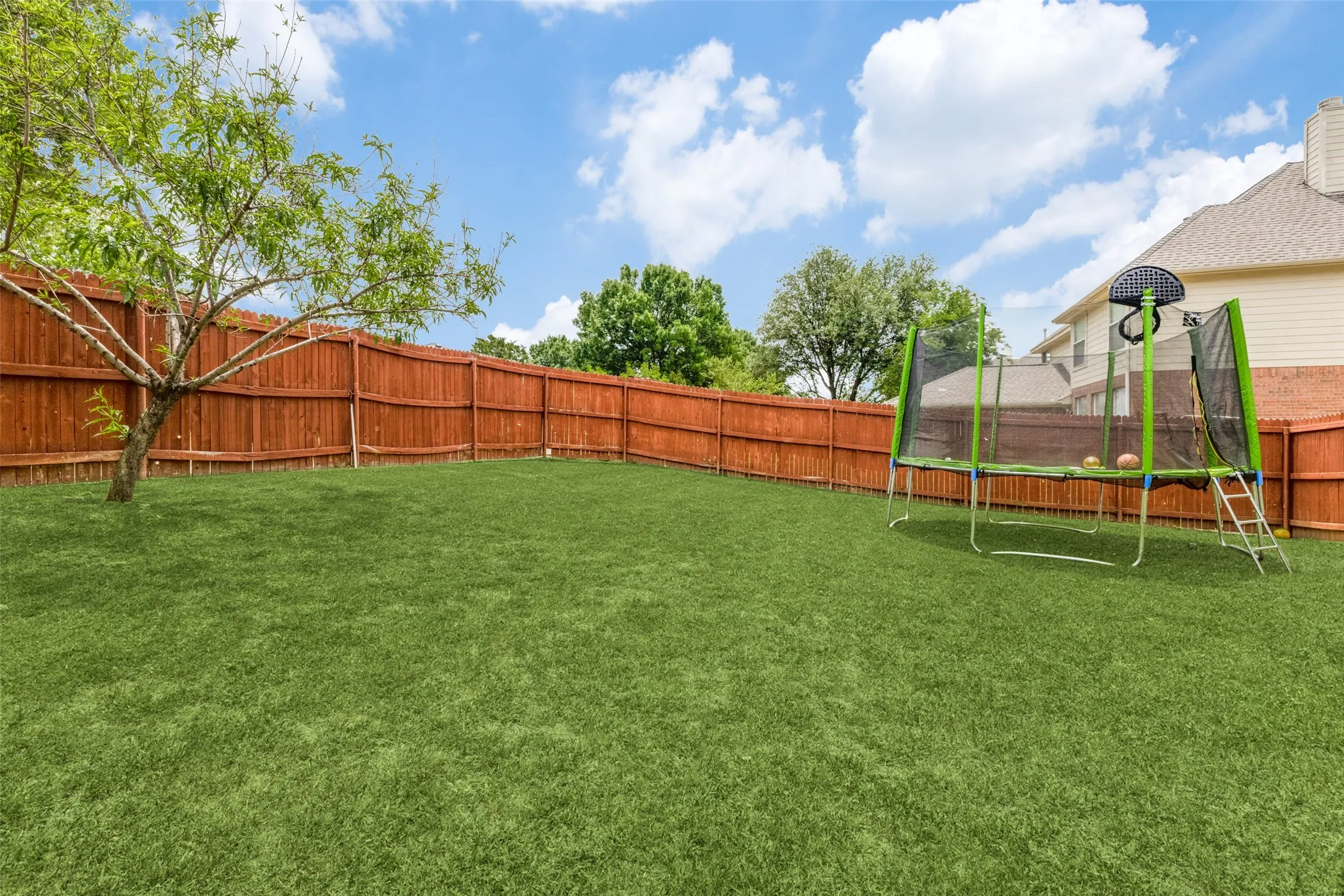 Expansive fenced backyard with a manicured lawn and mature tree