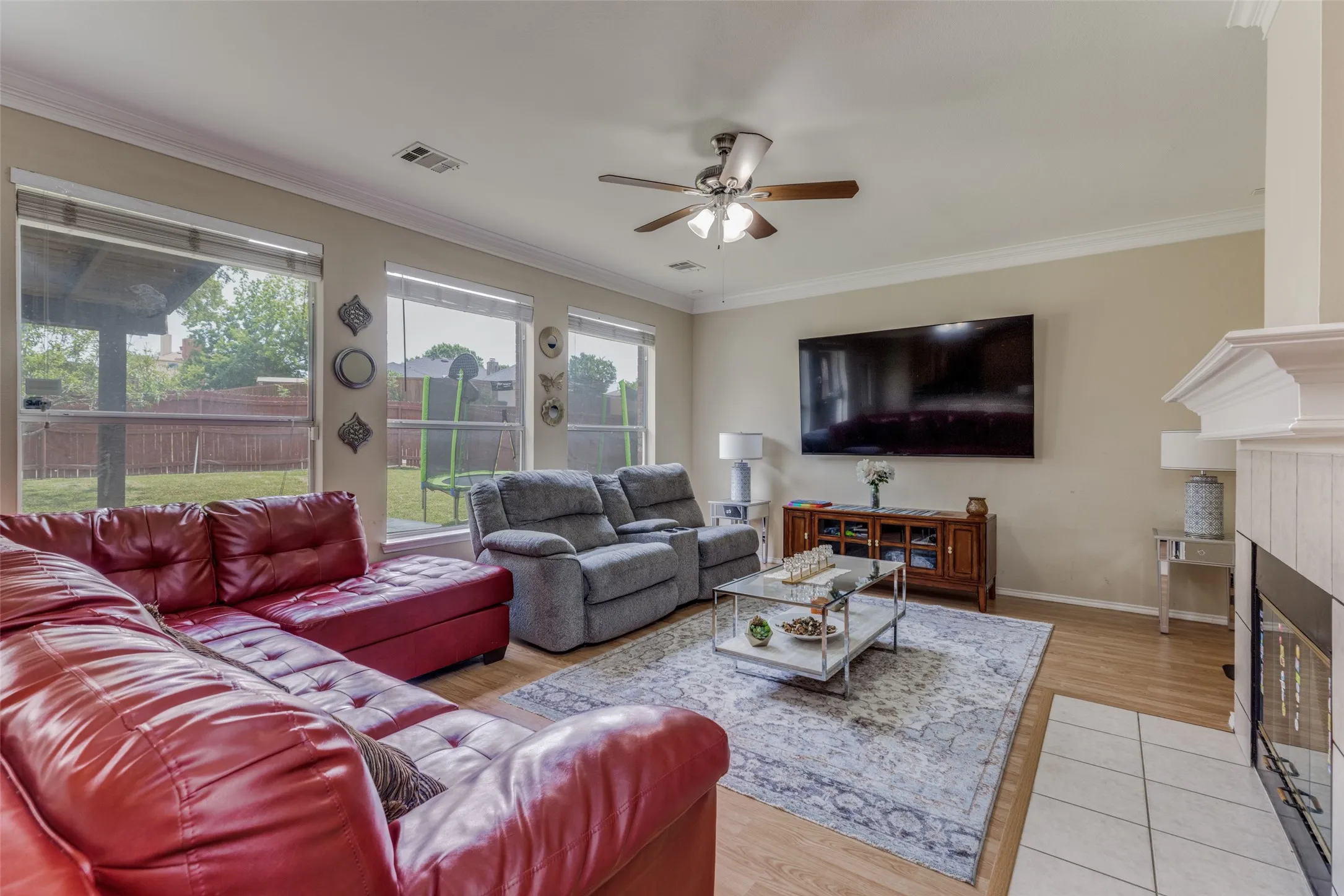 Recessed lighting and ceiling fan, wood-finish flooring, white fireplace surround with tile hearth, multiple windows, and crown​​‌​​​​‌​​‌‌​‌‌​​​‌‌​‌​‌​‌​​​‌​​ molding
