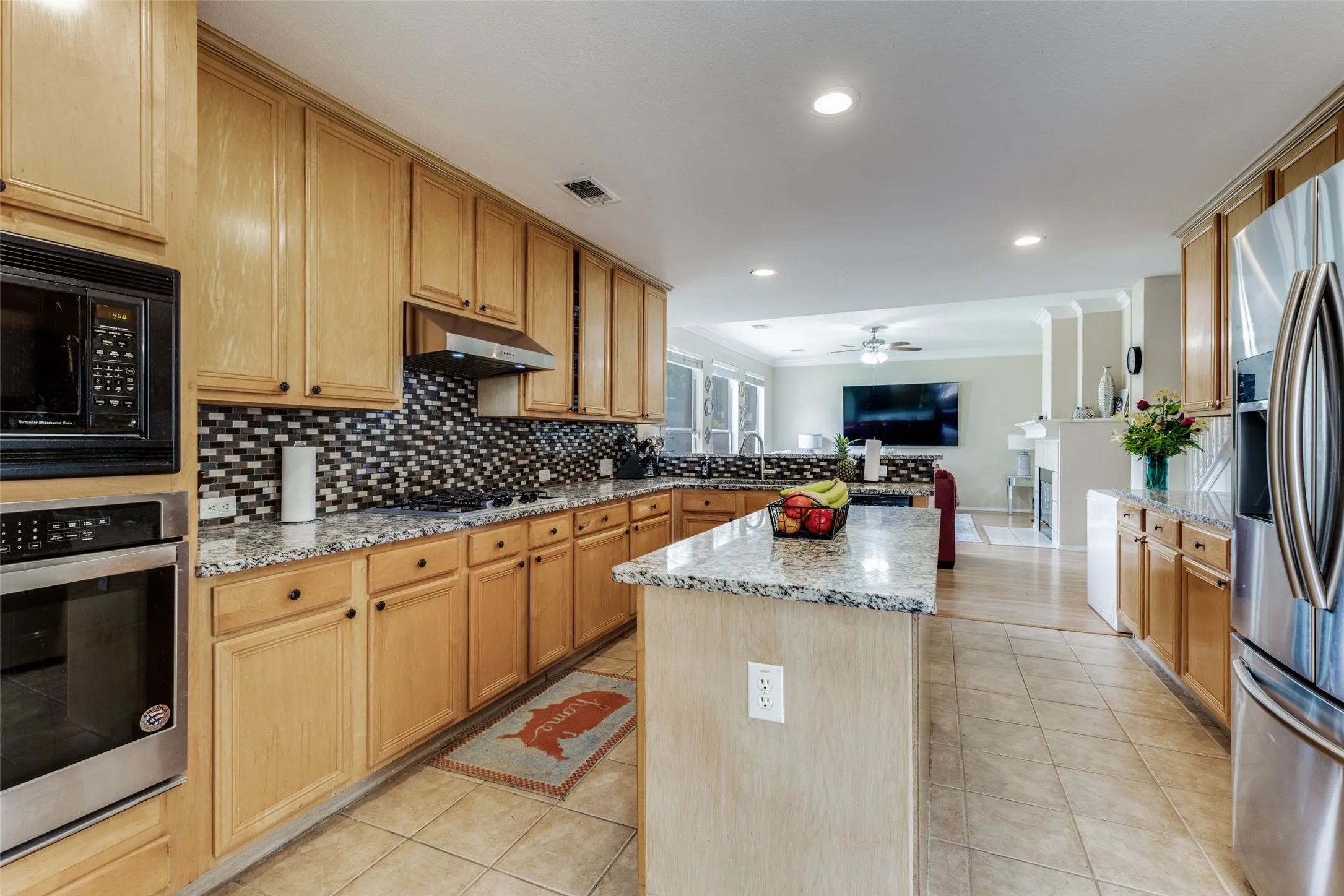 Kitchen featuring a built-in microwave and oven, a mosaic tile backsplash, granite countertops, and light wood-finish cabinetry