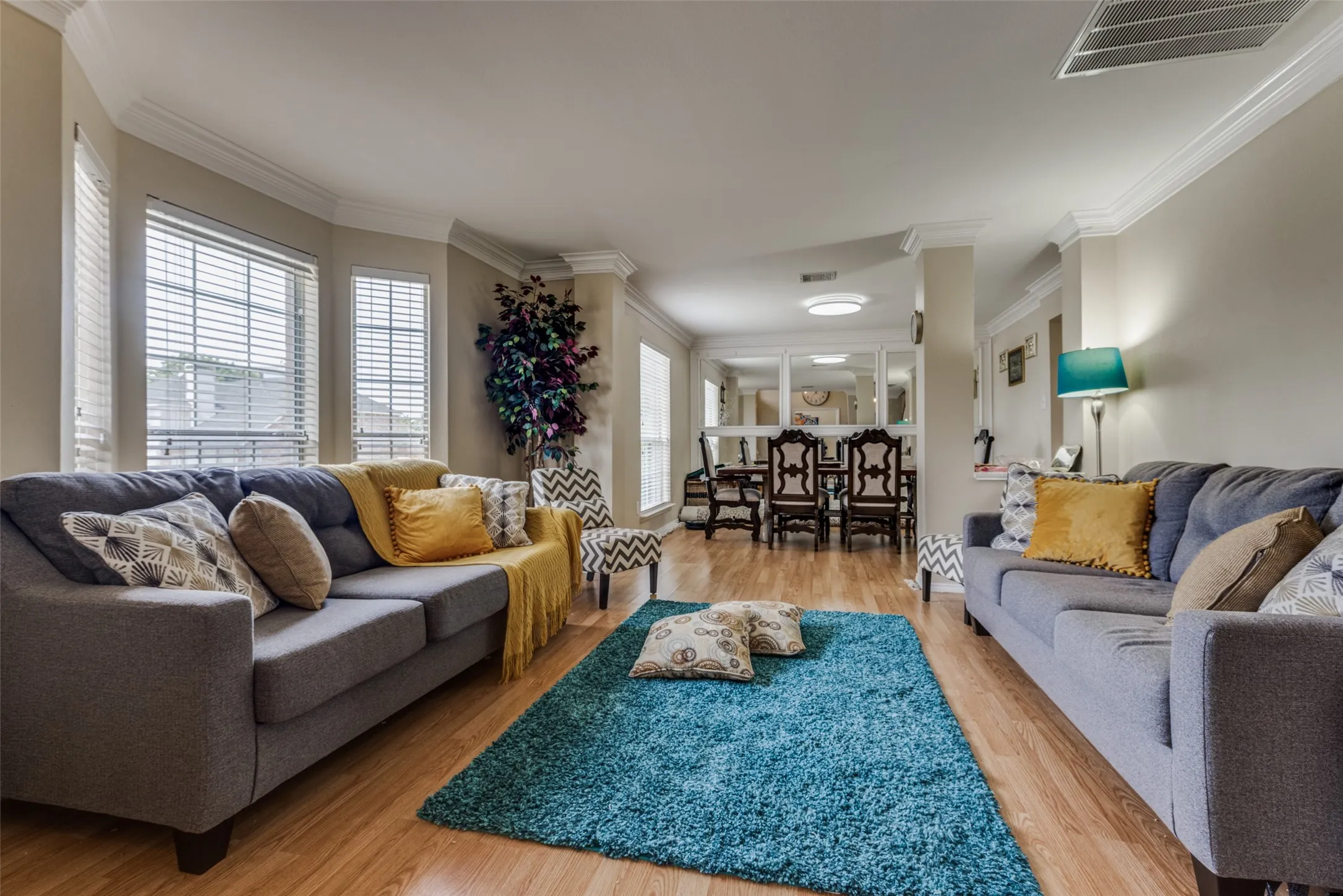 Living area featuring wood-finish flooring, crown molding, and a bay window with blinds