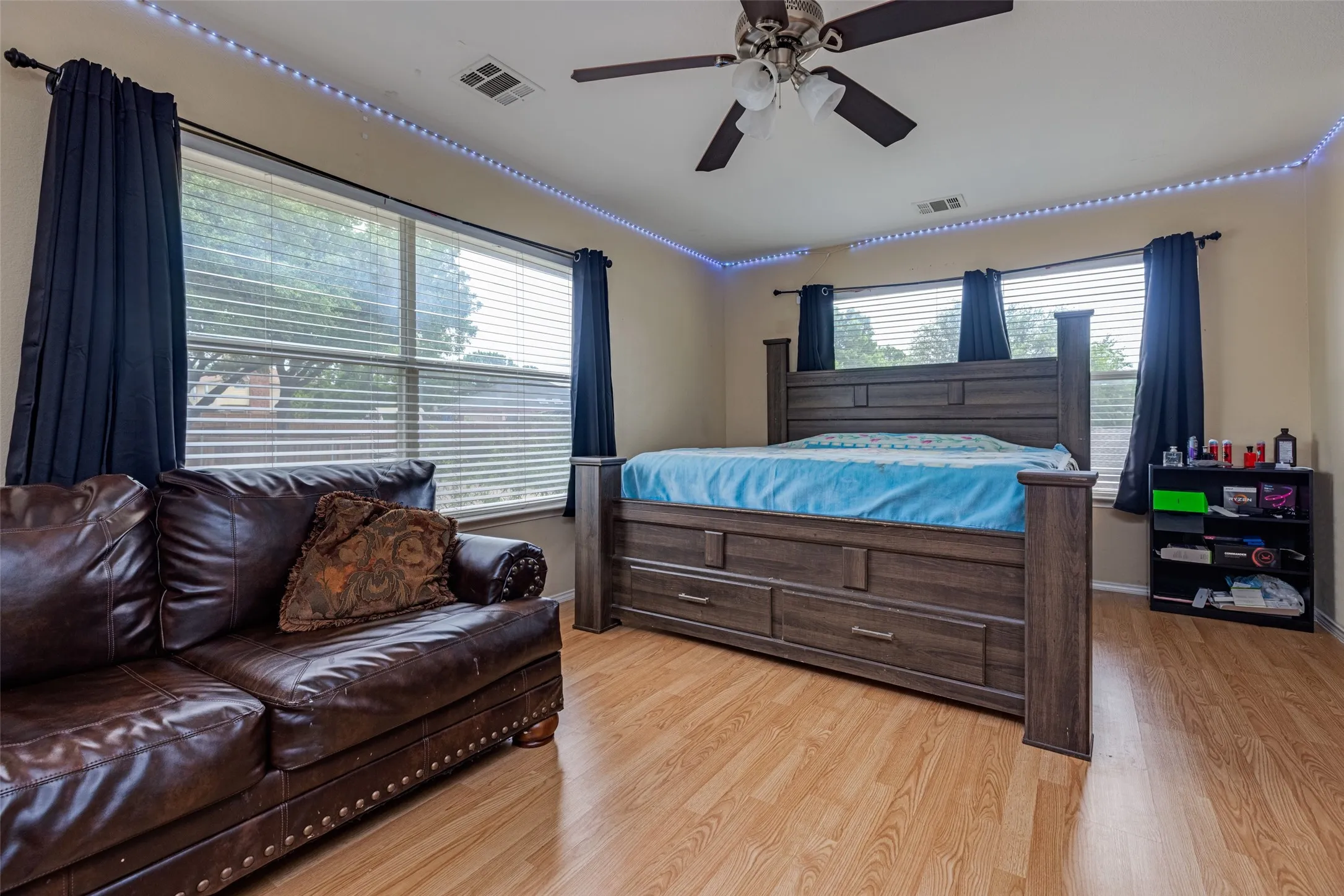 Wood-finish flooring, multiple windows with blinds, ceiling fan with integrated lighting, and perimeter lighting