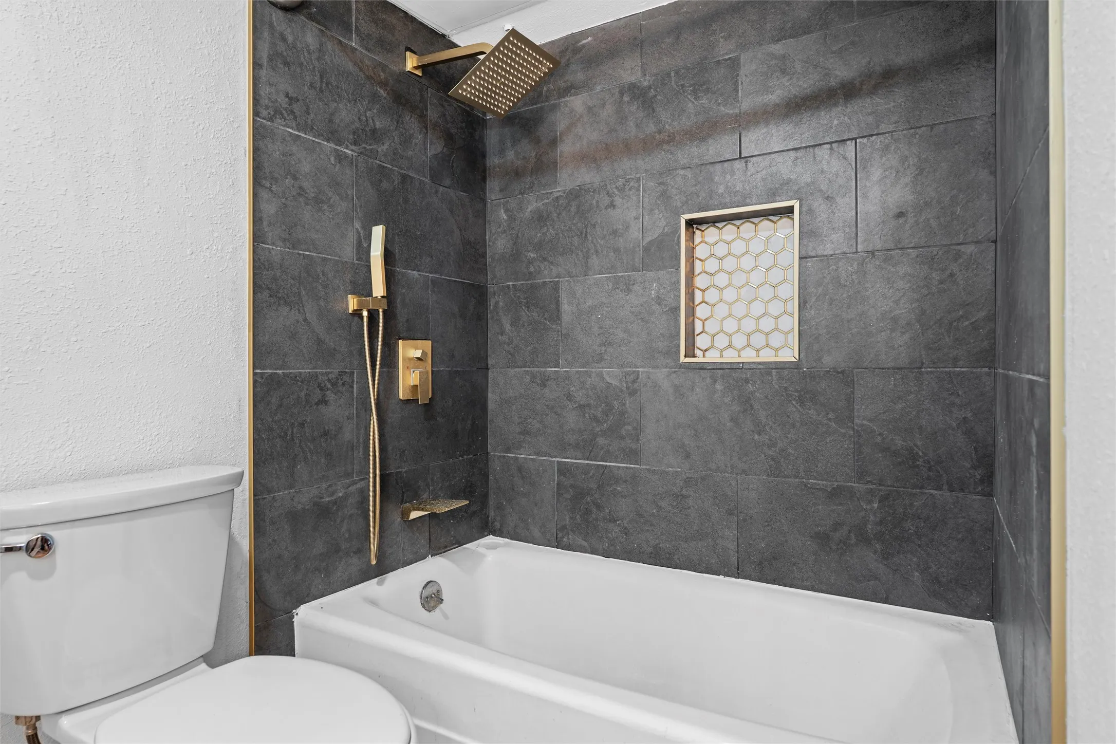 Spa-inspired bathroom featuring a soaking tub with polished brass fixtures, slate-tiled shower surround with integrated niche, rainfall showerhead, and a recessed medicine cabinet with integrated lighting