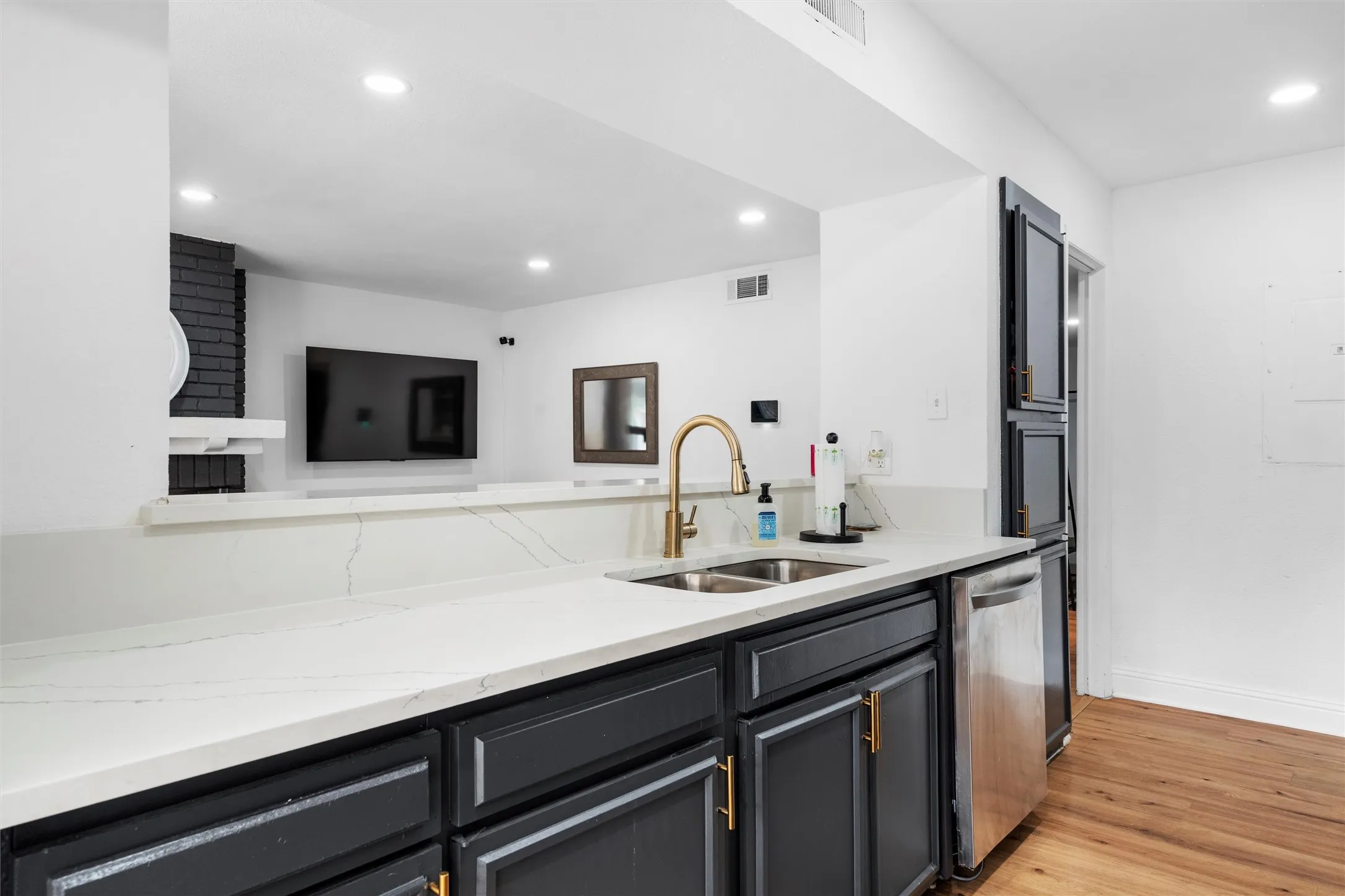 Modern kitchen featuring a large island with black cabinetry and brass hardware, white quartz countertops, stainless steel appliances, a brass gooseneck faucet, recessed ceiling lighting, and warm wood-finish flooring throughout