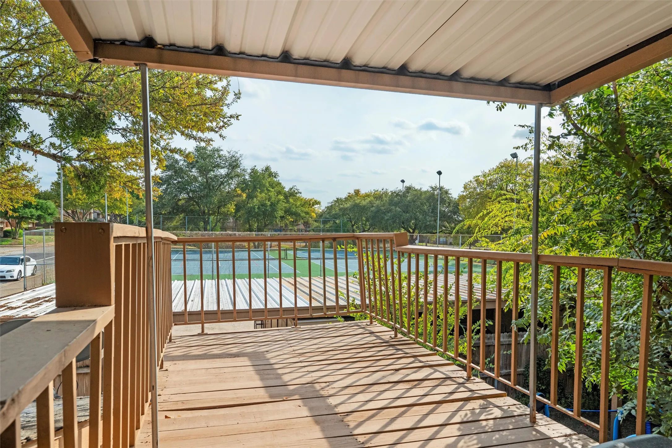 Upper Covered deck with railings overlooking tennis courts and surrounding landscaping