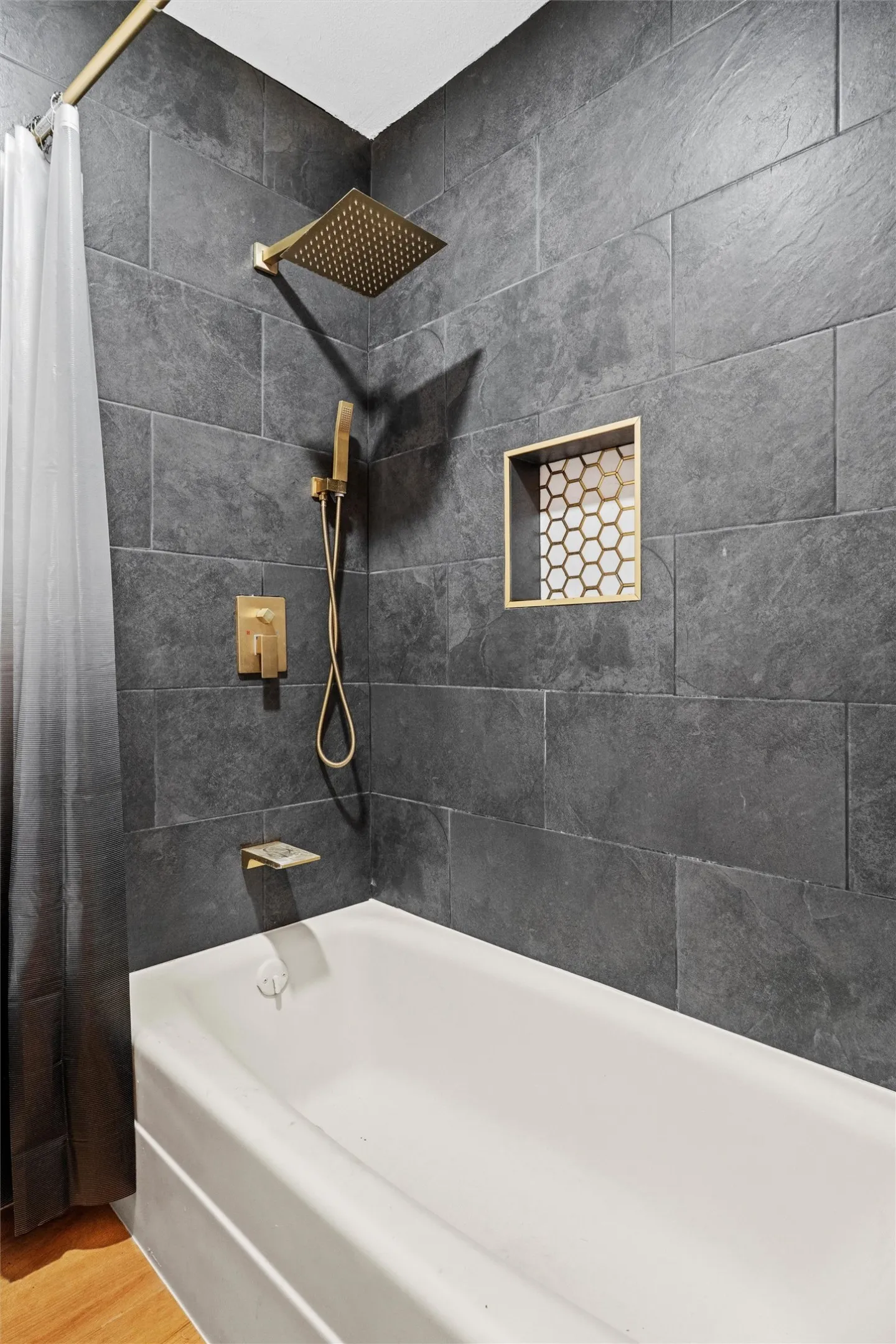 Modern spa-inspired bathroom featuring large-format slate tile walls, a white soaking tub, and premium brass fixtures including a rainfall showerhead and handheld sprayer