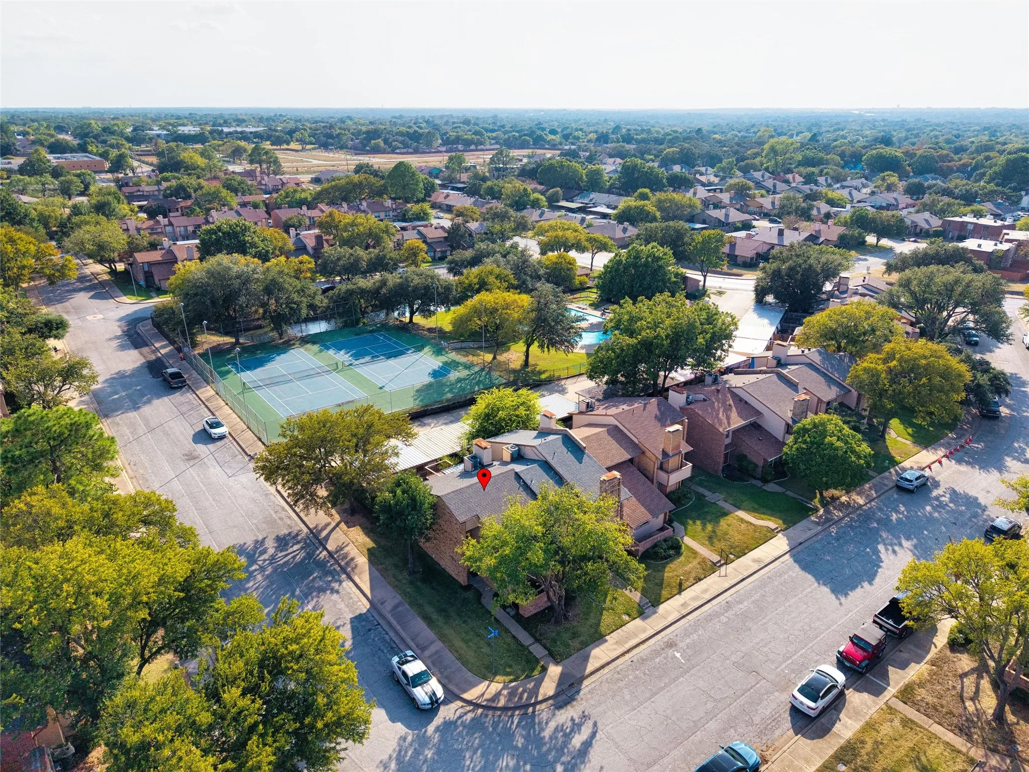 Aerial view showcasing a brick residence with mature landscaping on a corner lot, featuring a resort-style swimming pool with surrounding hardscape, multiple parking spaces, and tree-lined streetscapes throughout the established neighborhood