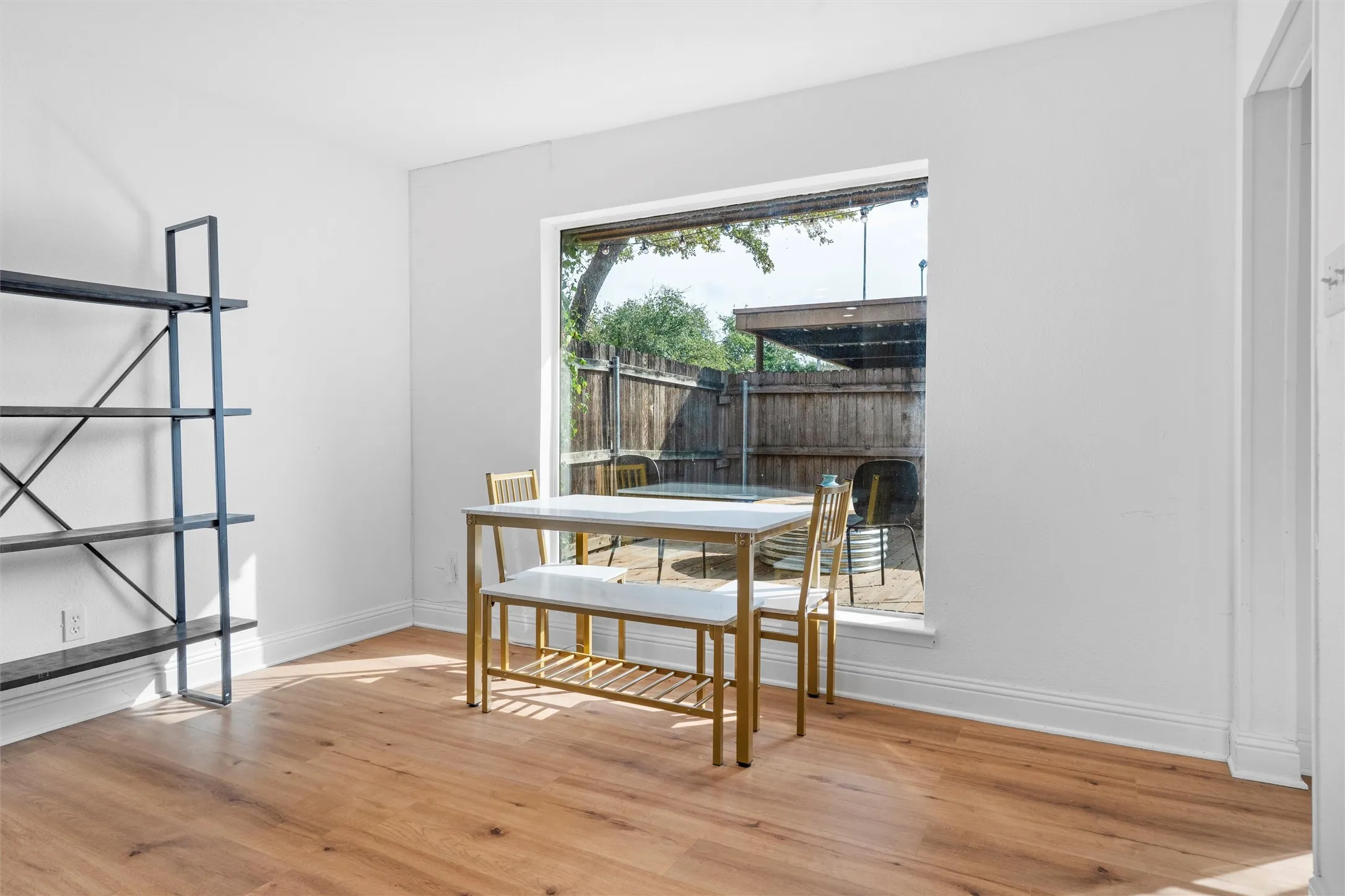 Bright interior space featuring warm wood-finish flooring, floor-to-ceiling glass doors opening to a private outdoor patio, white walls, and industrial-style metal shelving