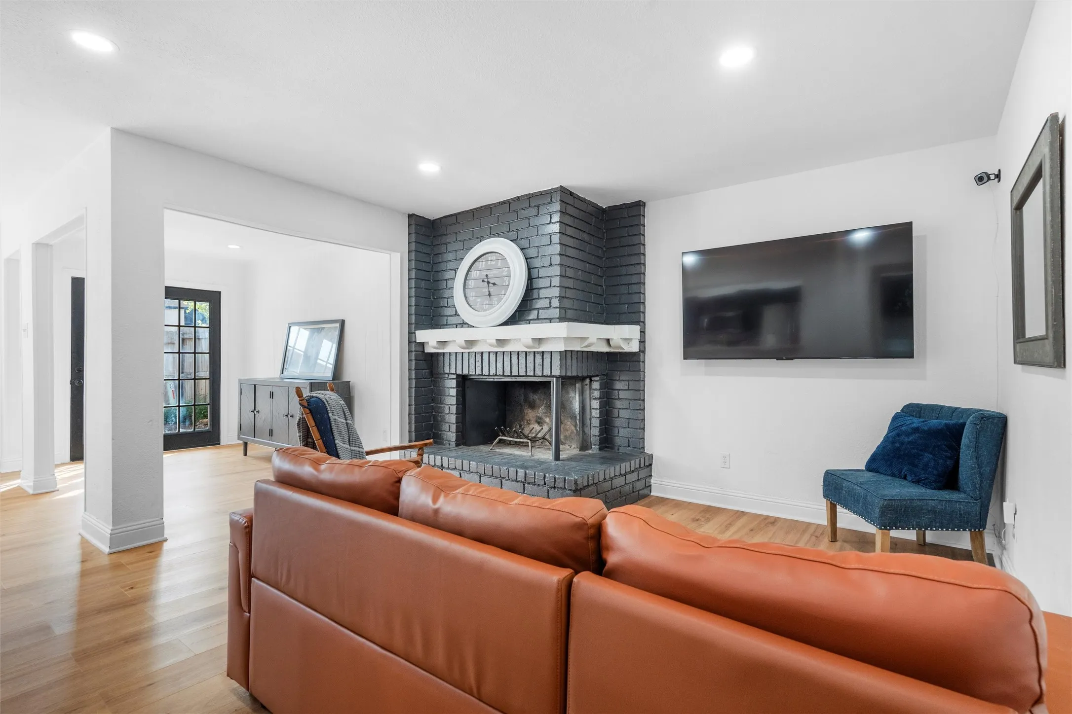 Contemporary living room featuring a wood-finish floor, custom leather sectional seating, and a striking brick fireplace with built-in mantelpiece
