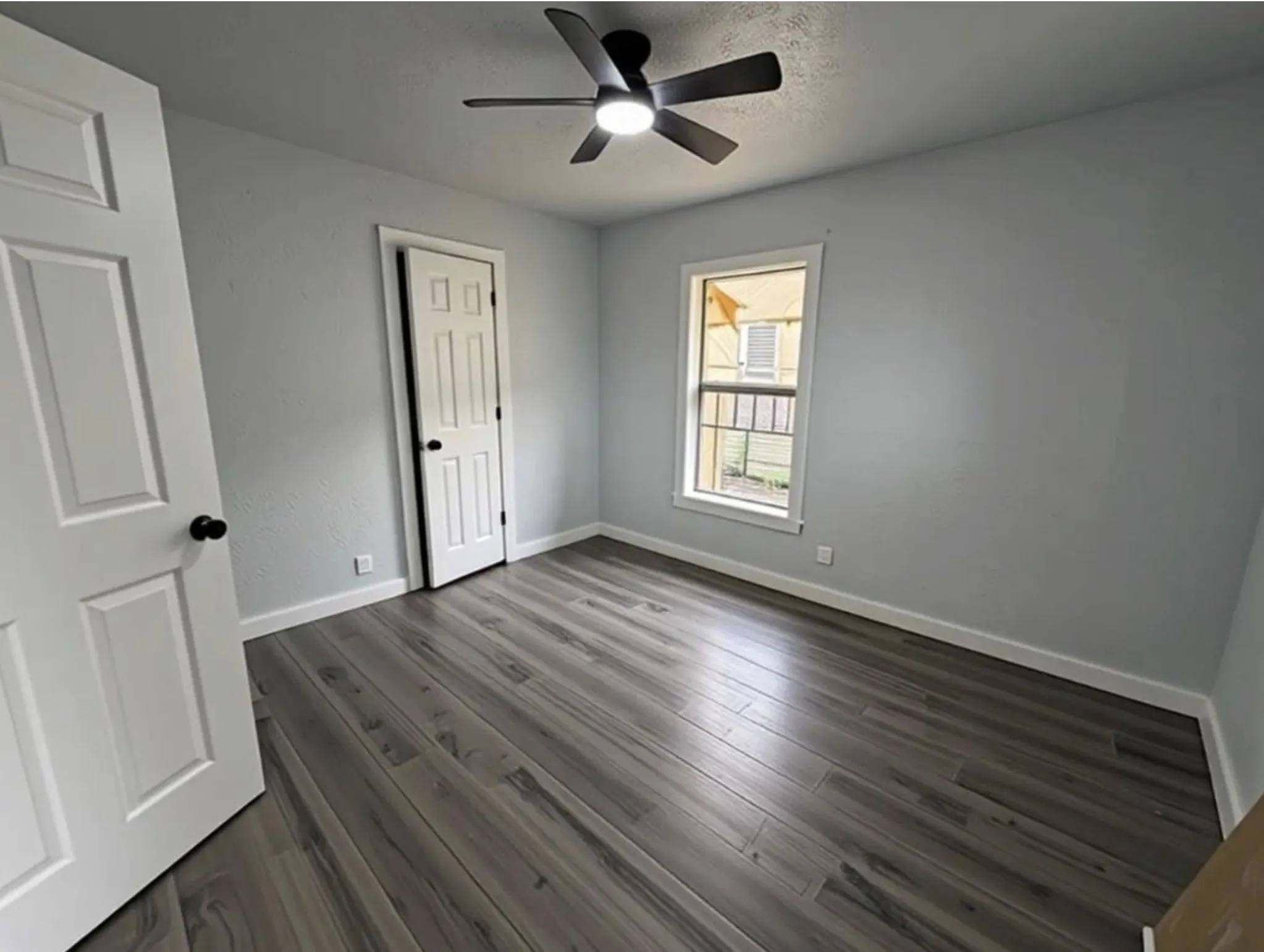 Wood-finish flooring, ceiling fan, white paneled doors, and a window with trim