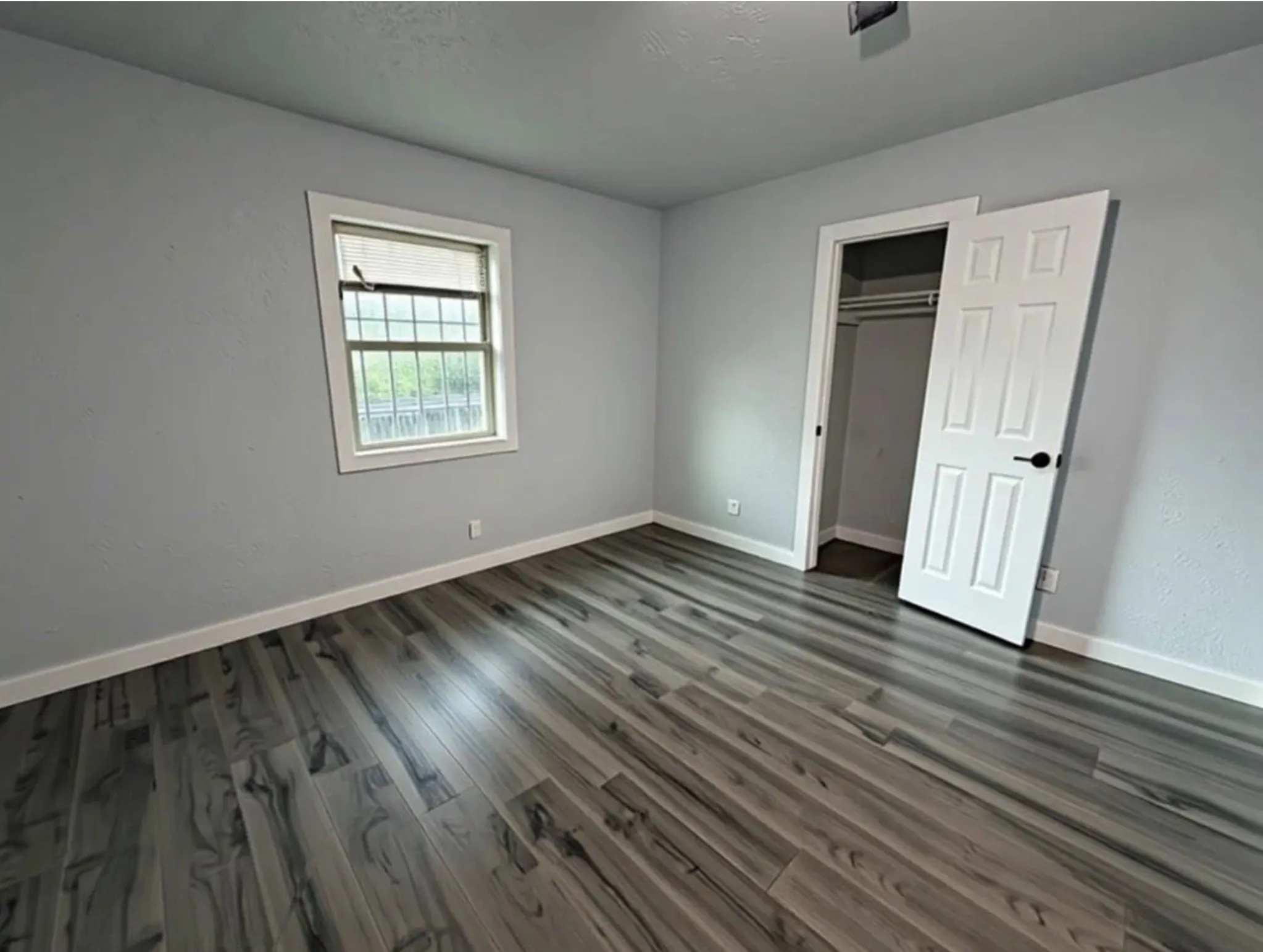 Wood-finish flooring, light gray wall finishes, a white-framed window with security bars, and a white paneled door with black hardware