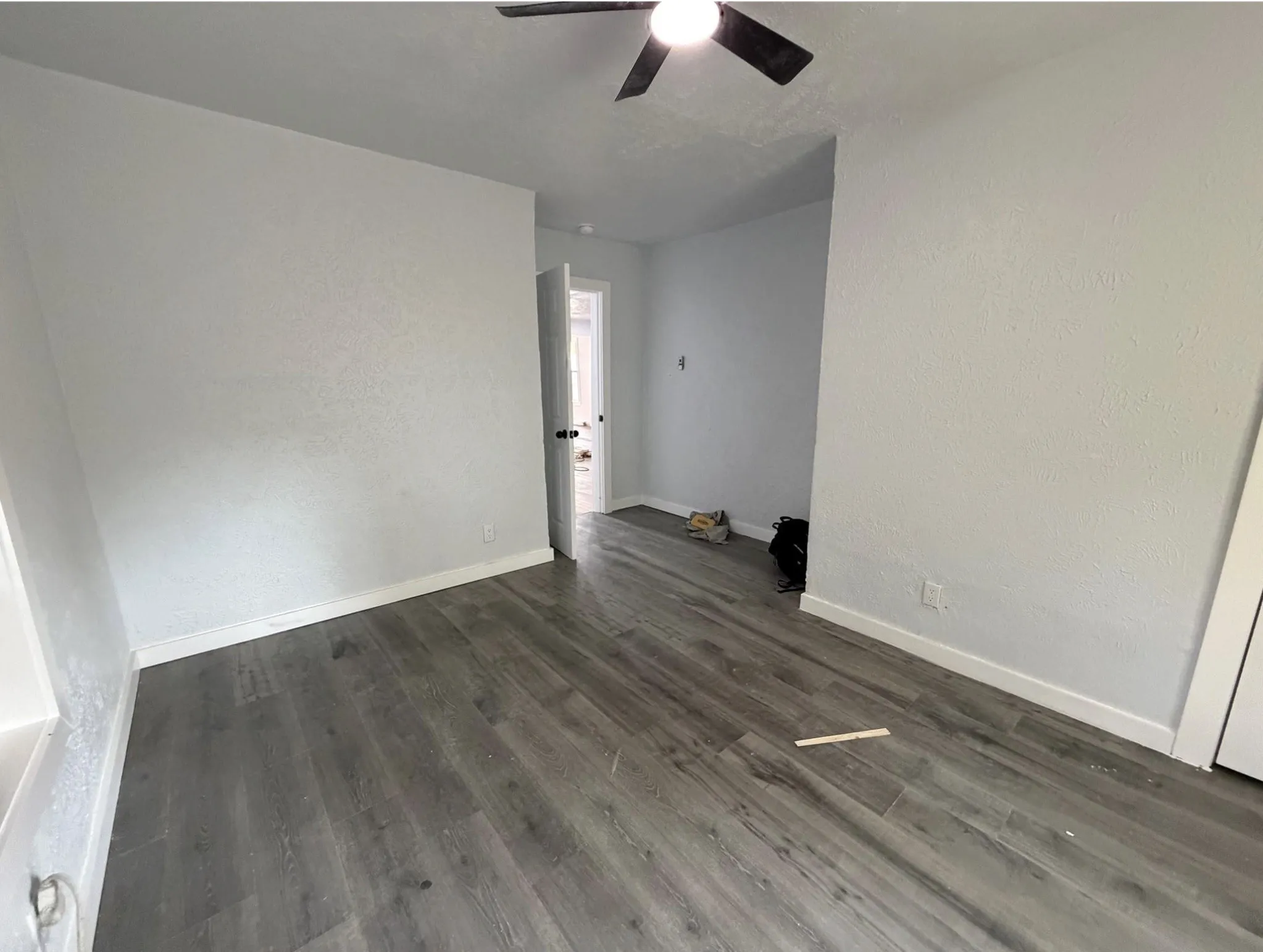 Wood-finish flooring with white trim, ceiling fan light fixture, and white painted walls