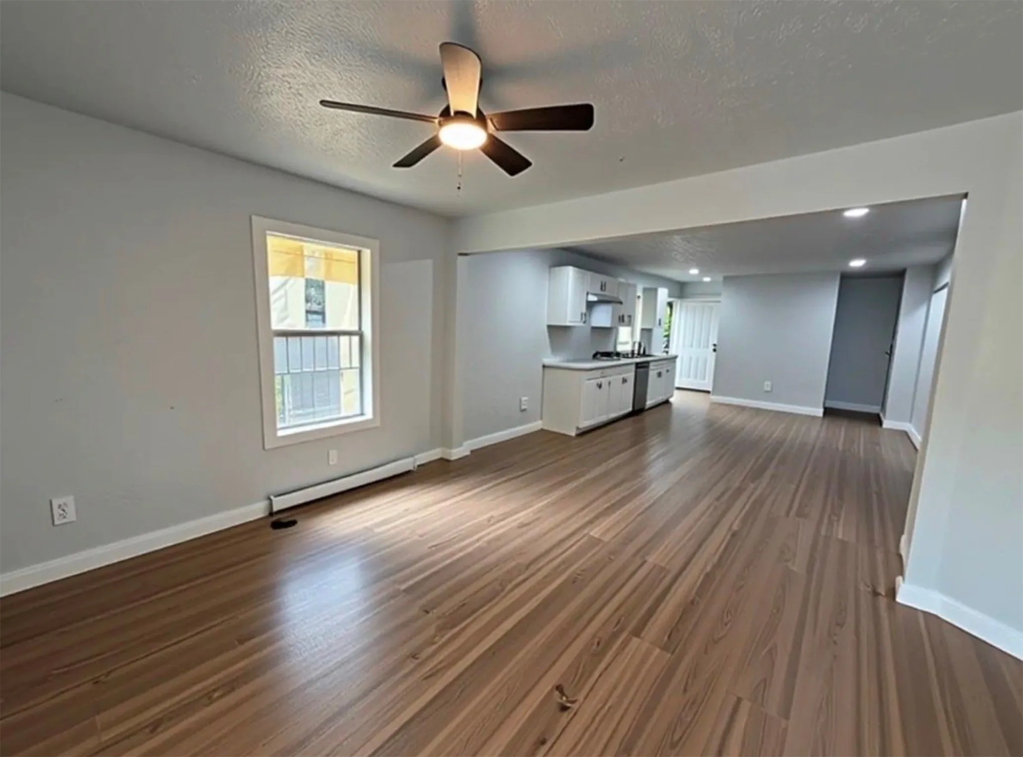 Wood-finish flooring throughout, light gray wall color, a ceiling fan with integrated lighting, recessed lighting, and white cabinetry