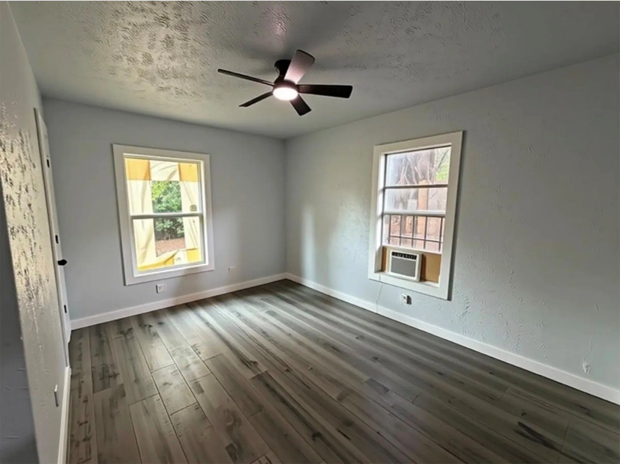 Wood-finish flooring, ceiling fan with integrated lighting, multiple windows, and crisp white trim