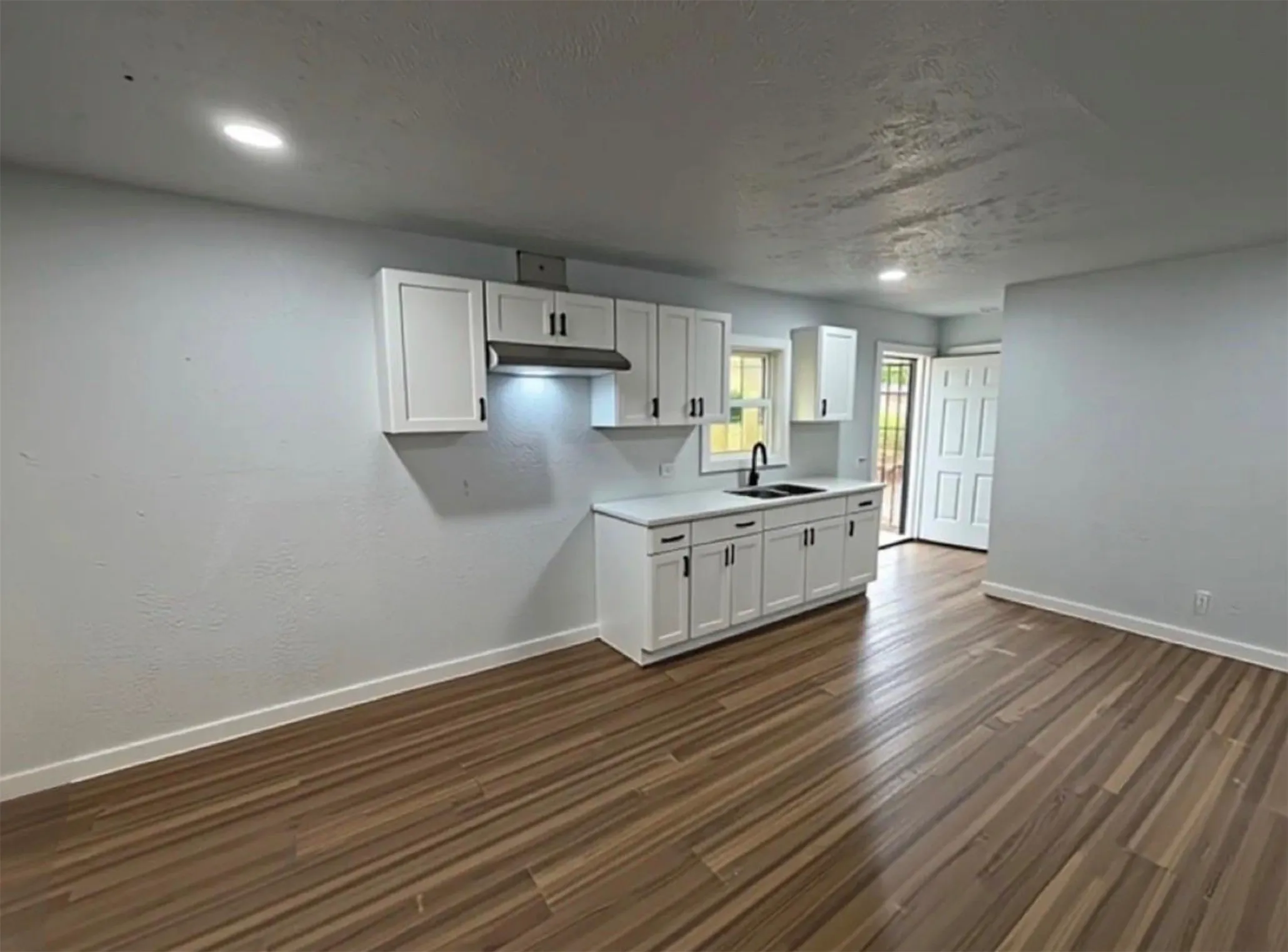 Wood-finish flooring throughout, white cabinetry with matte black hardware, recessed lighting, and a black sink with a matching faucet