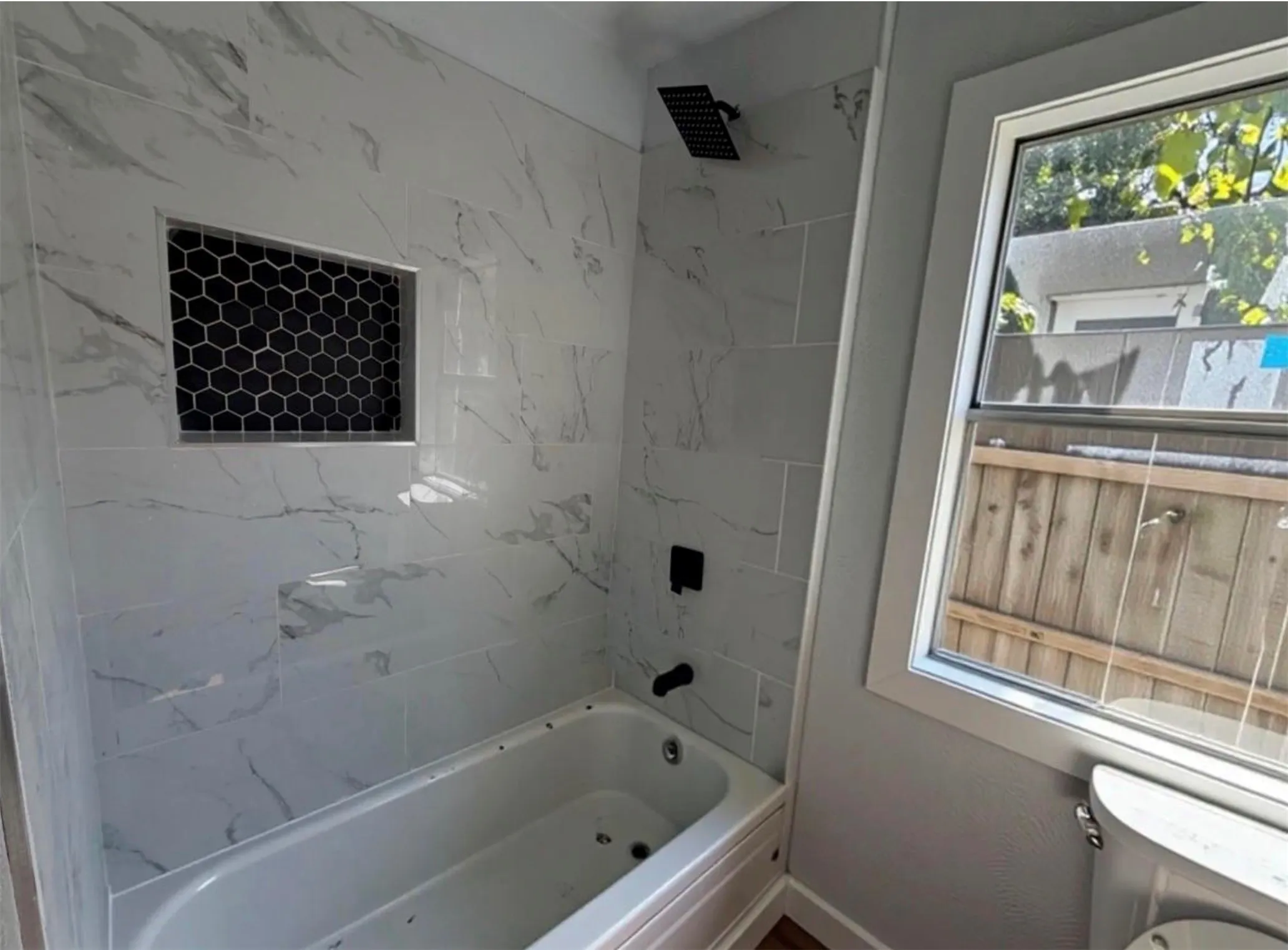 Bathtub with tiled surround, black hexagonal tile shower niche, and matte black fixtures