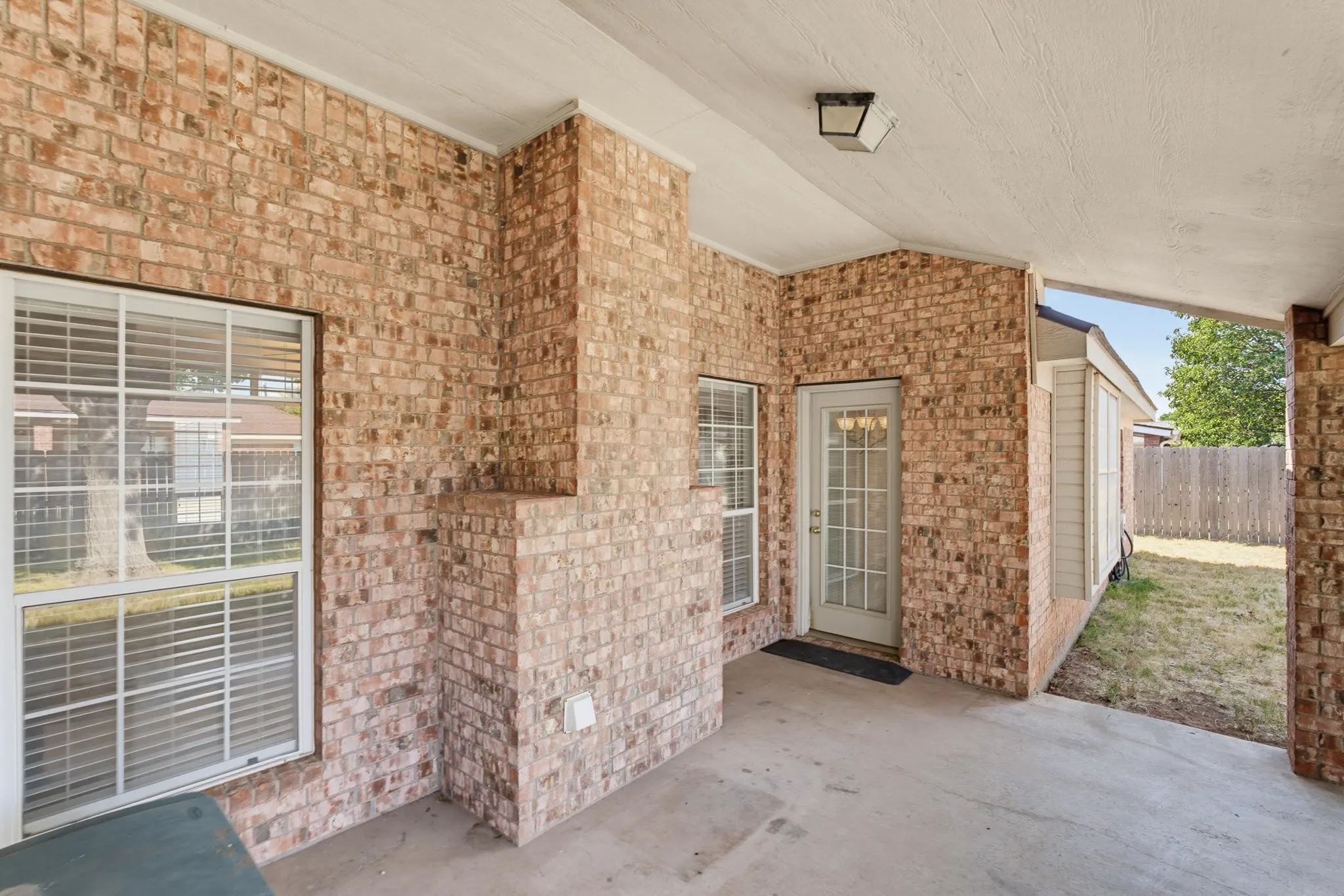 Covered patio featuring brick walls, a concrete floor, a white paneled door with glass inserts, and a flush-mount ceiling light fixture