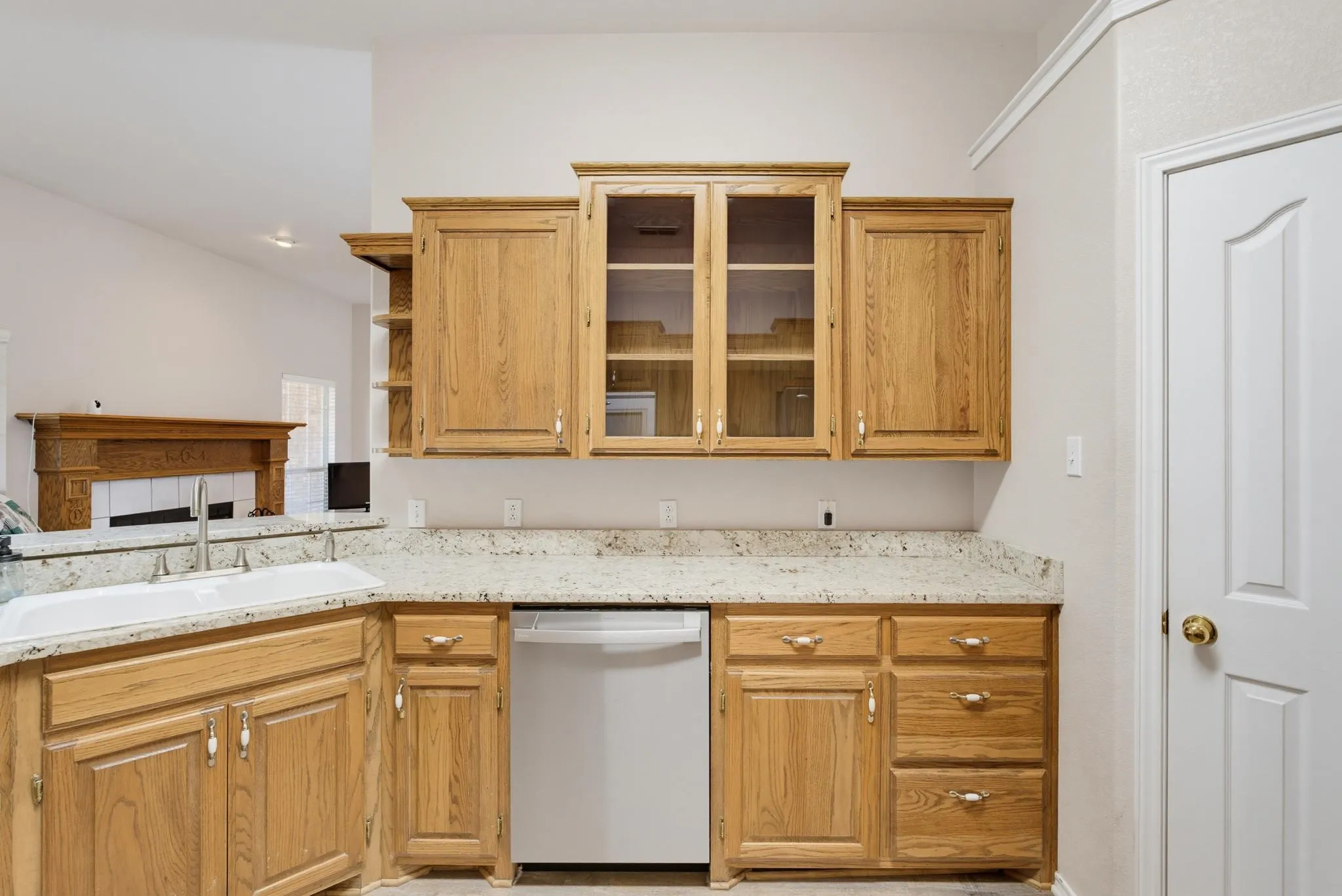 Kitchen featuring wood cabinetry, light-toned countertops, a white undermount sink with a gooseneck faucet, and a paneled white dishwasher