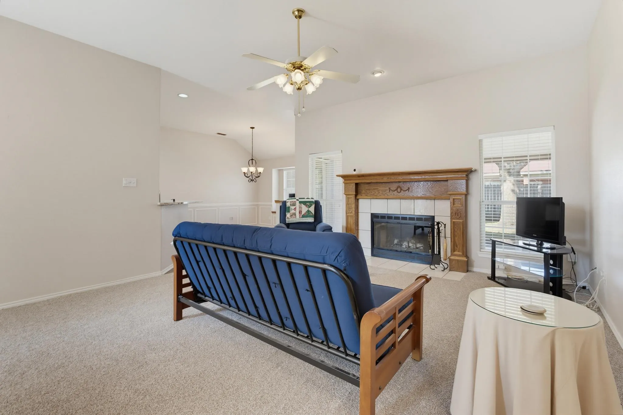 Vaulted ceiling, ceiling fan with integrated lighting, wood mantel, tiled fireplace surround, and recessed lighting