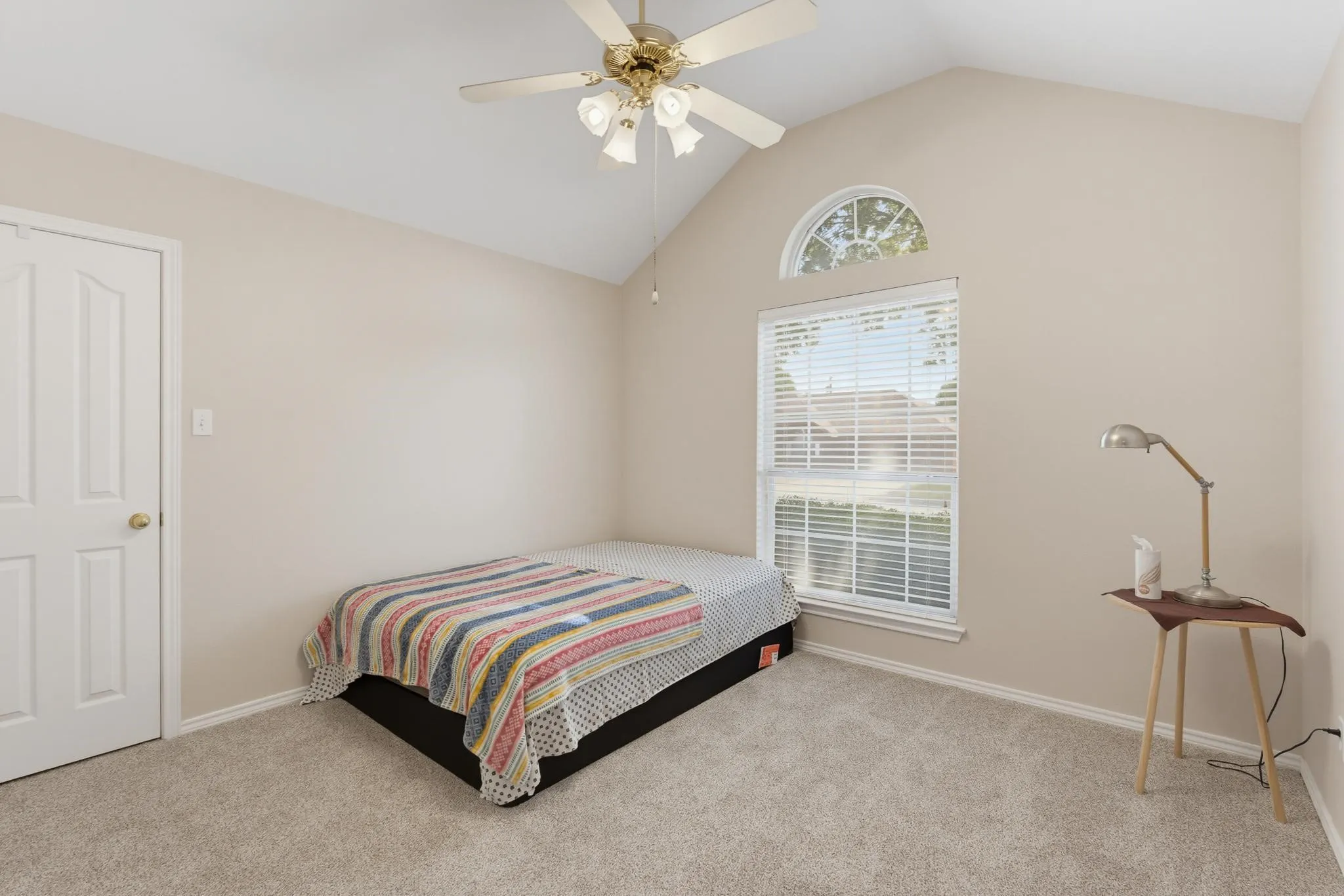 Vaulted ceiling featuring a ceiling fan, arched transom window, and a double-hung window with blinds, all set above plush carpet flooring