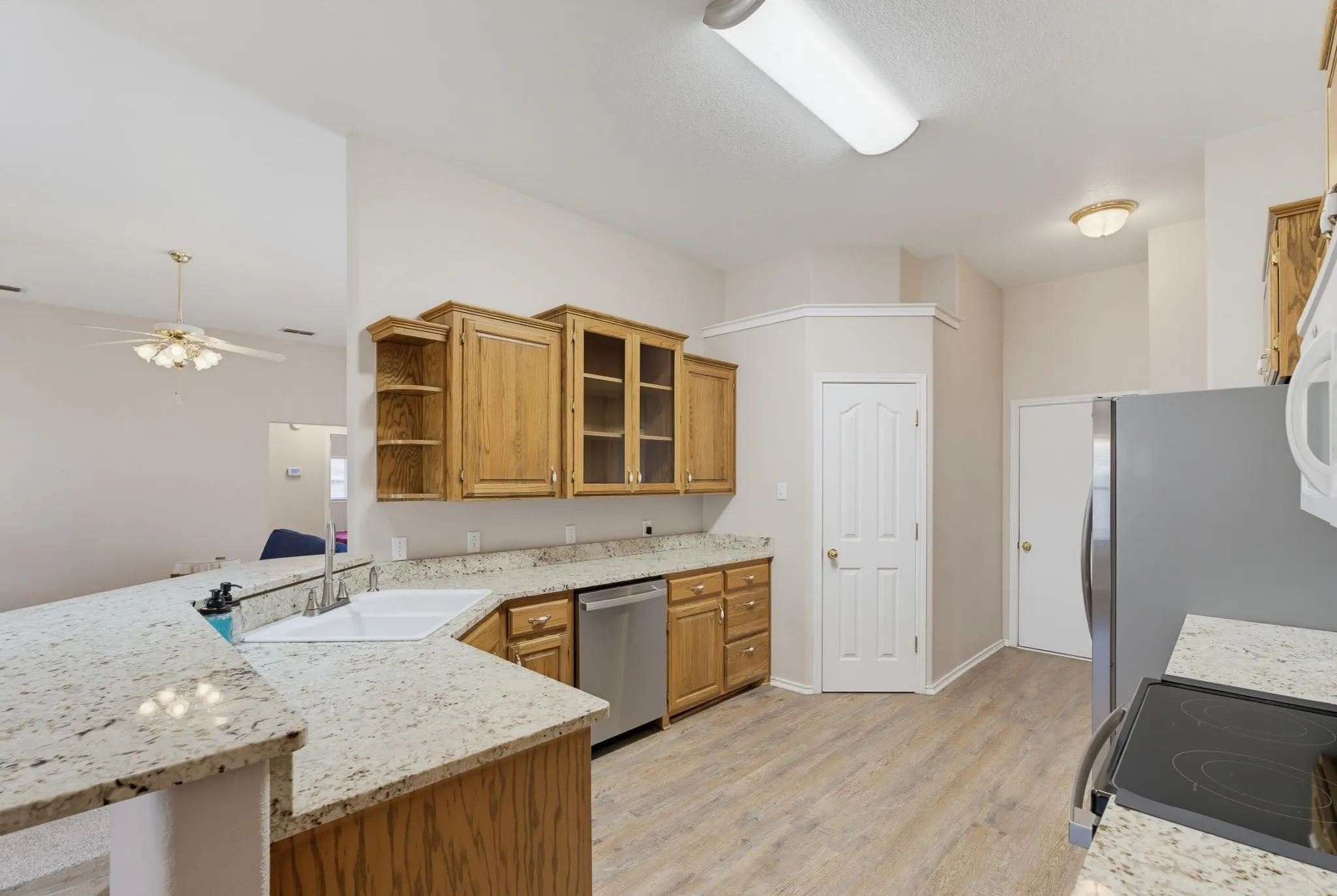 Kitchen featuring wood-finish flooring, wood cabinetry, stone countertops, and a stainless-steel dishwasher