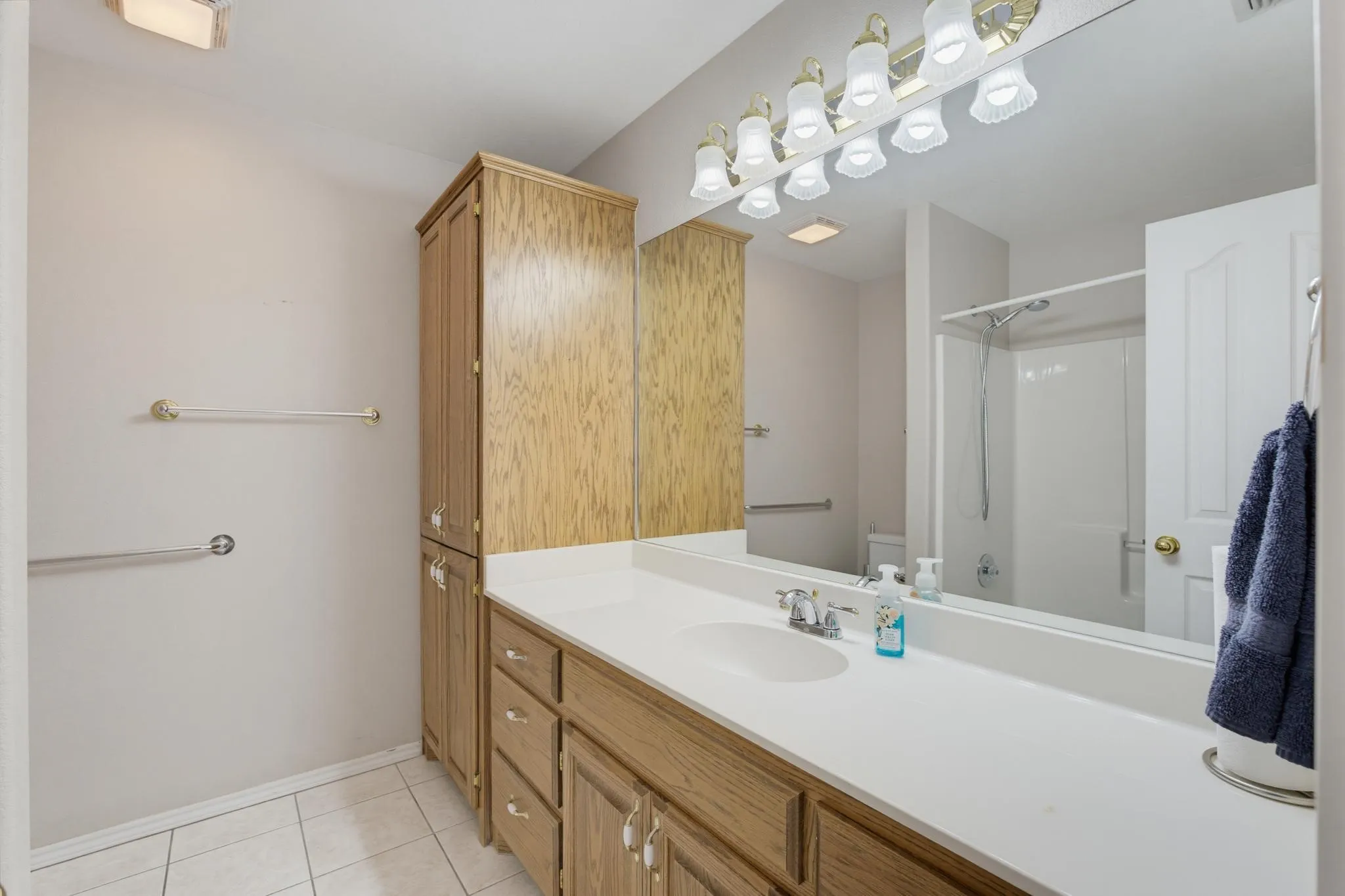 Long vanity with an integrated sink, wood-finish cabinetry, and a large wall-mounted mirror