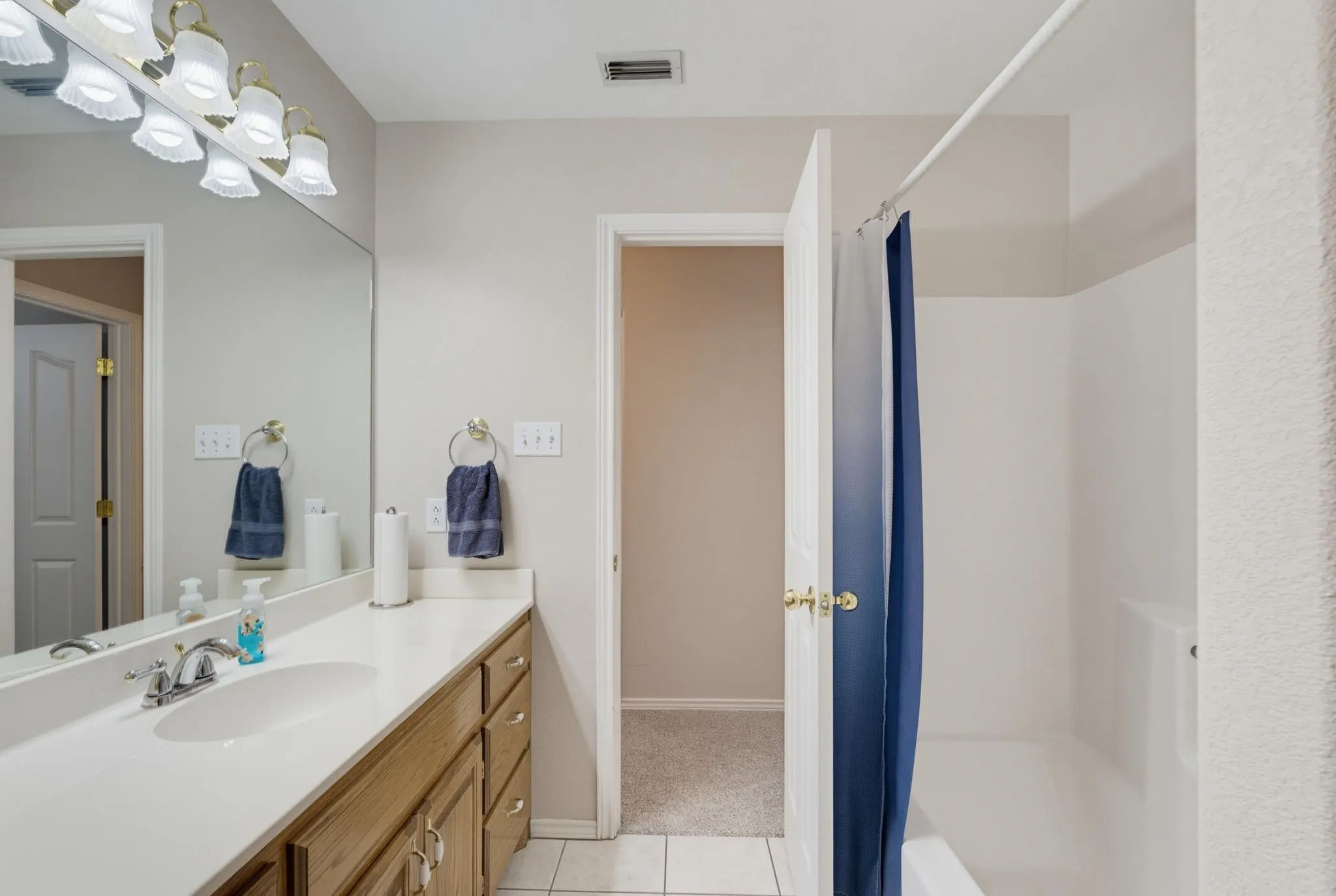 Bathroom featuring a white tile floor, a single vanity with wood-finish cabinetry, a white countertop, and an integrated sink with a chrome faucet