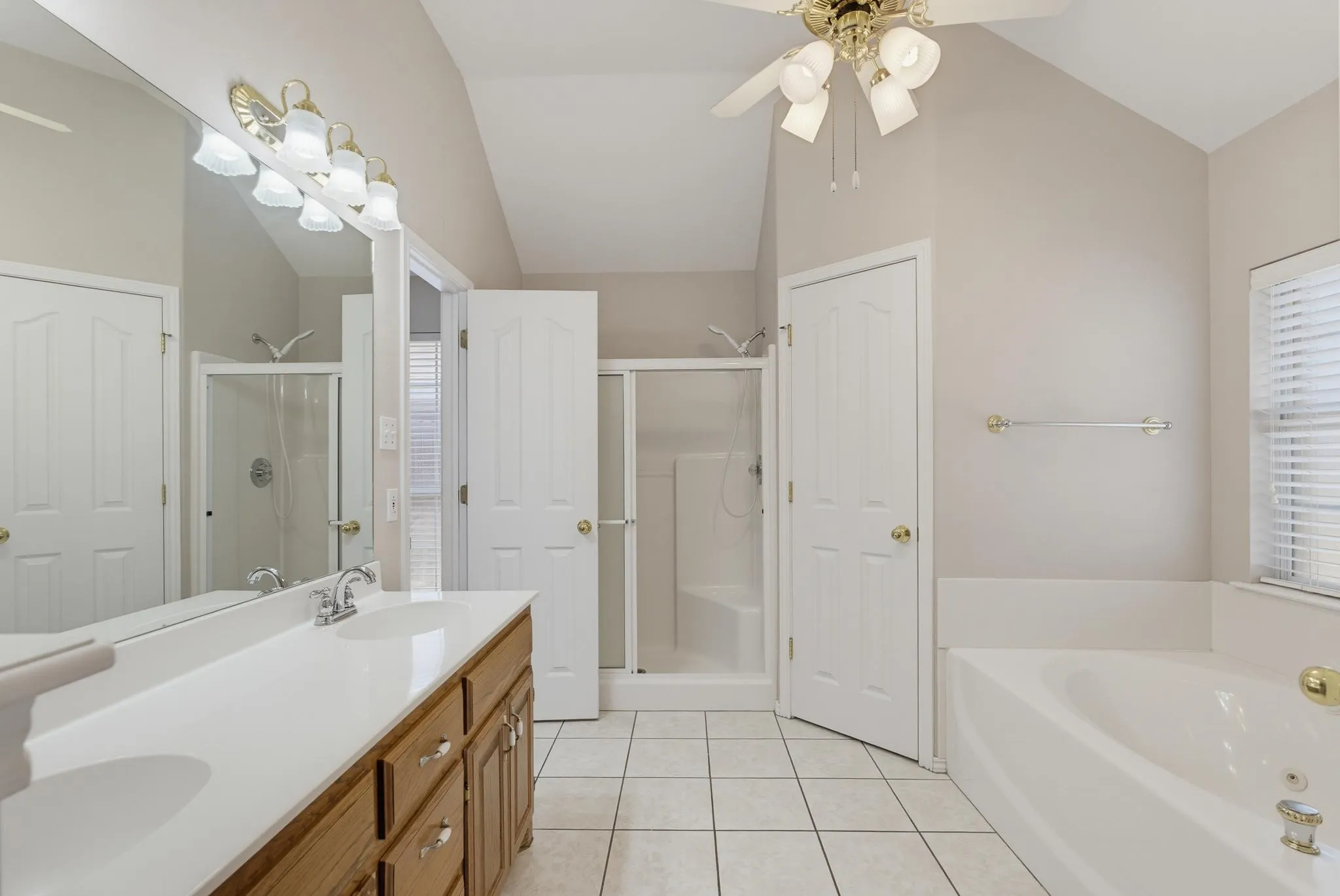 Vaulted ceiling bathroom featuring a double vanity with wood cabinetry, a built-in tub, a separate shower, and tiled flooring