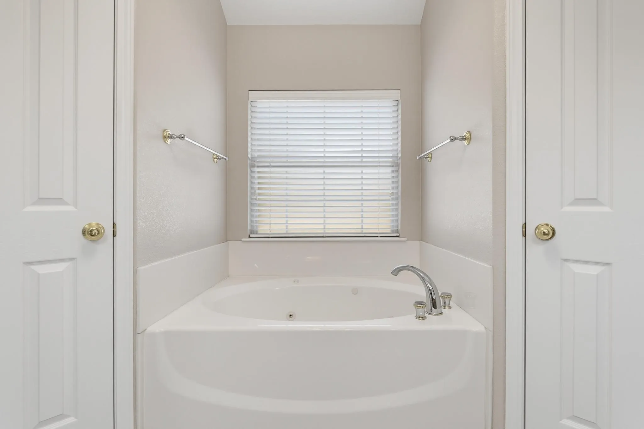 Corner soaking tub with chrome fixtures, framed by two panel doors and a window with horizontal blinds