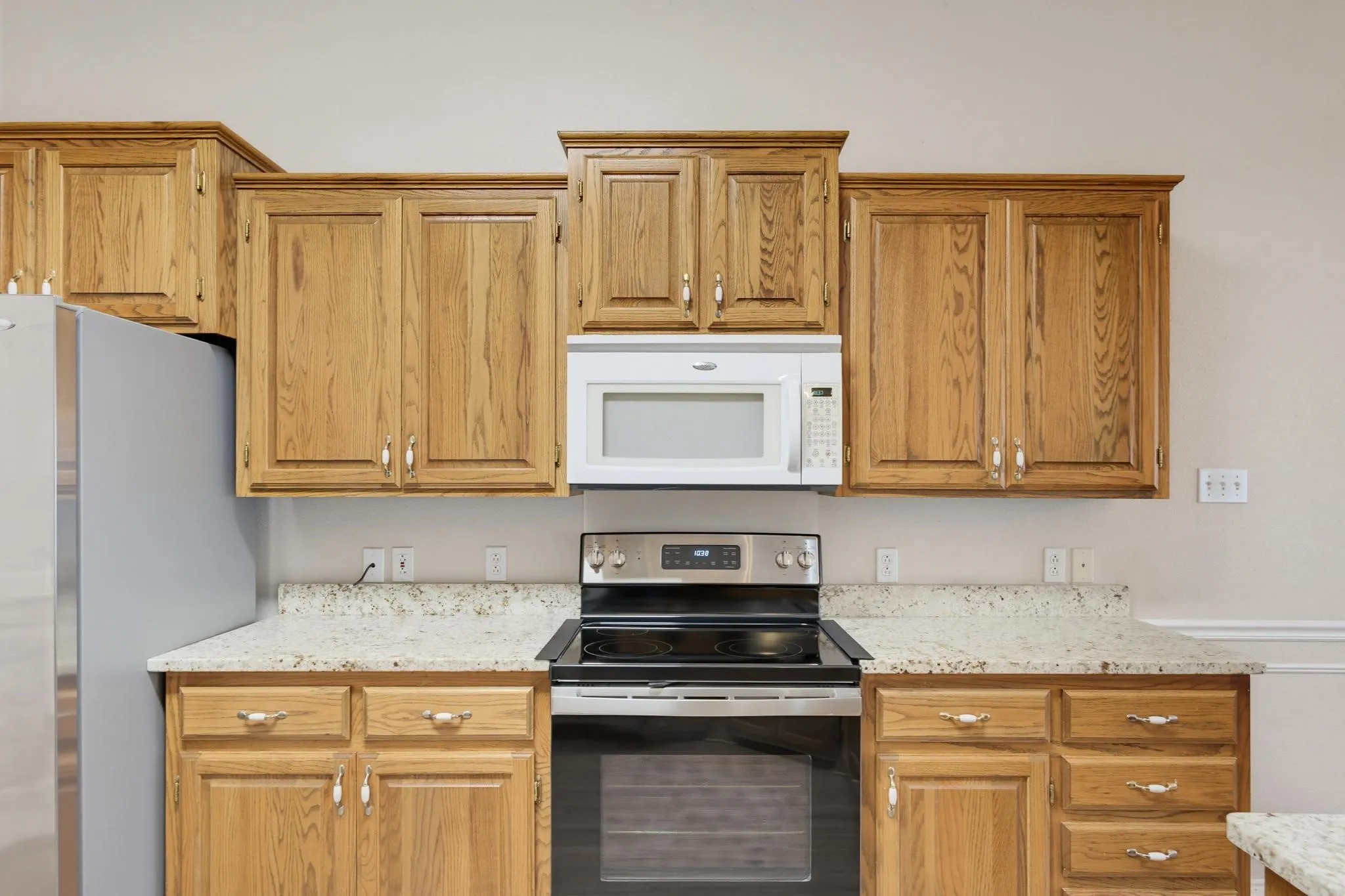 Kitchen with wood-finish cabinetry, light-toned countertops, stainless steel electric range, and a white built-in microwave