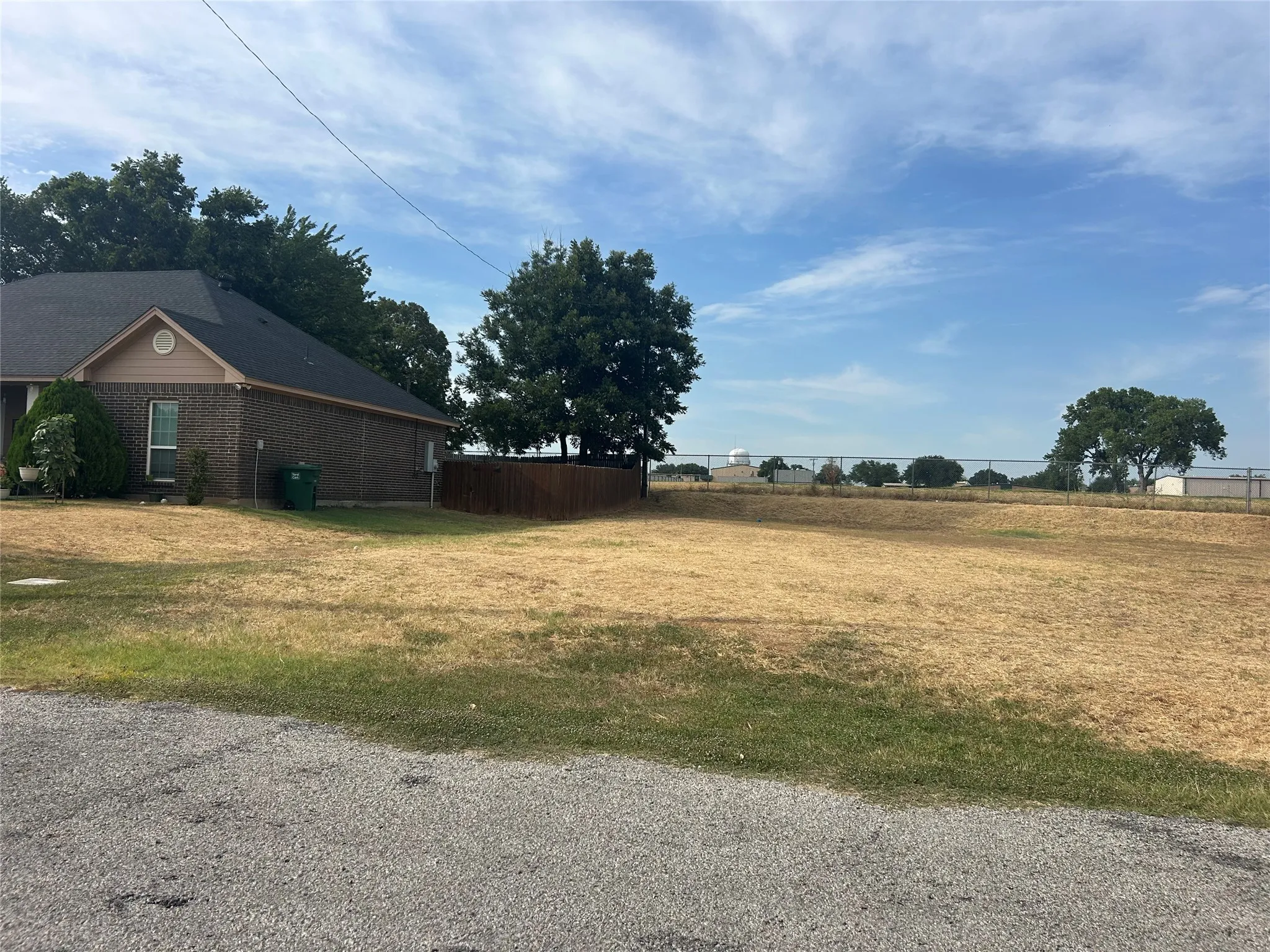 Expansive lot with partial wood fencing, mature trees, and gravel road frontage