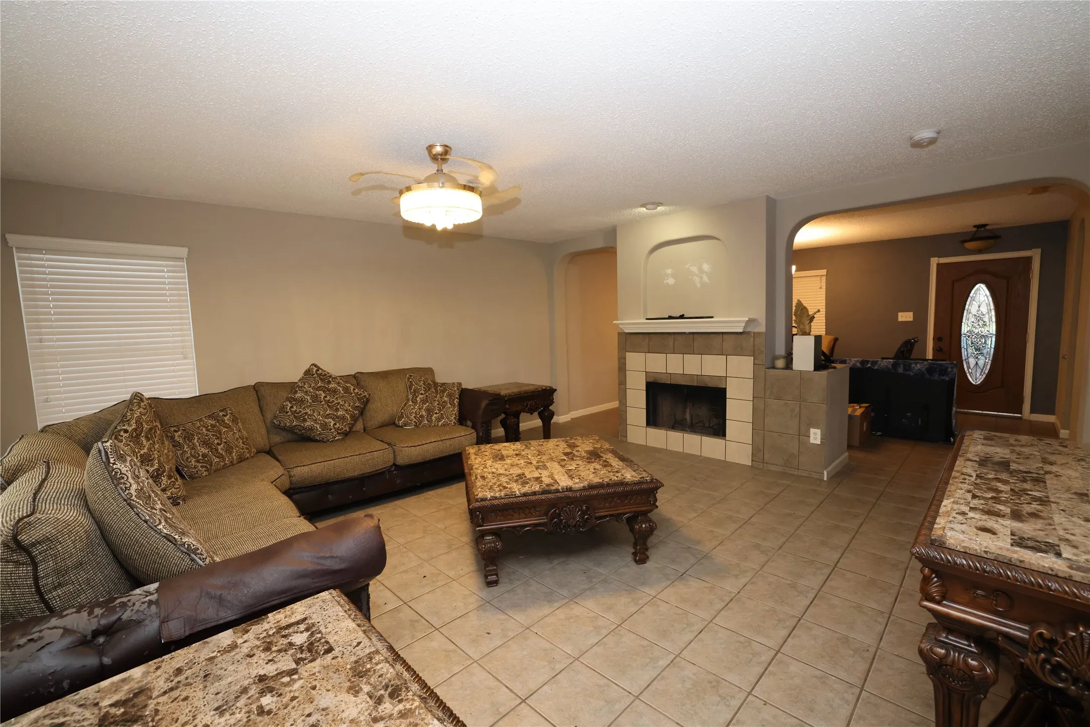 Tile flooring, built-in fireplace with tile surround, arched doorway, and ceiling fan with integrated lighting