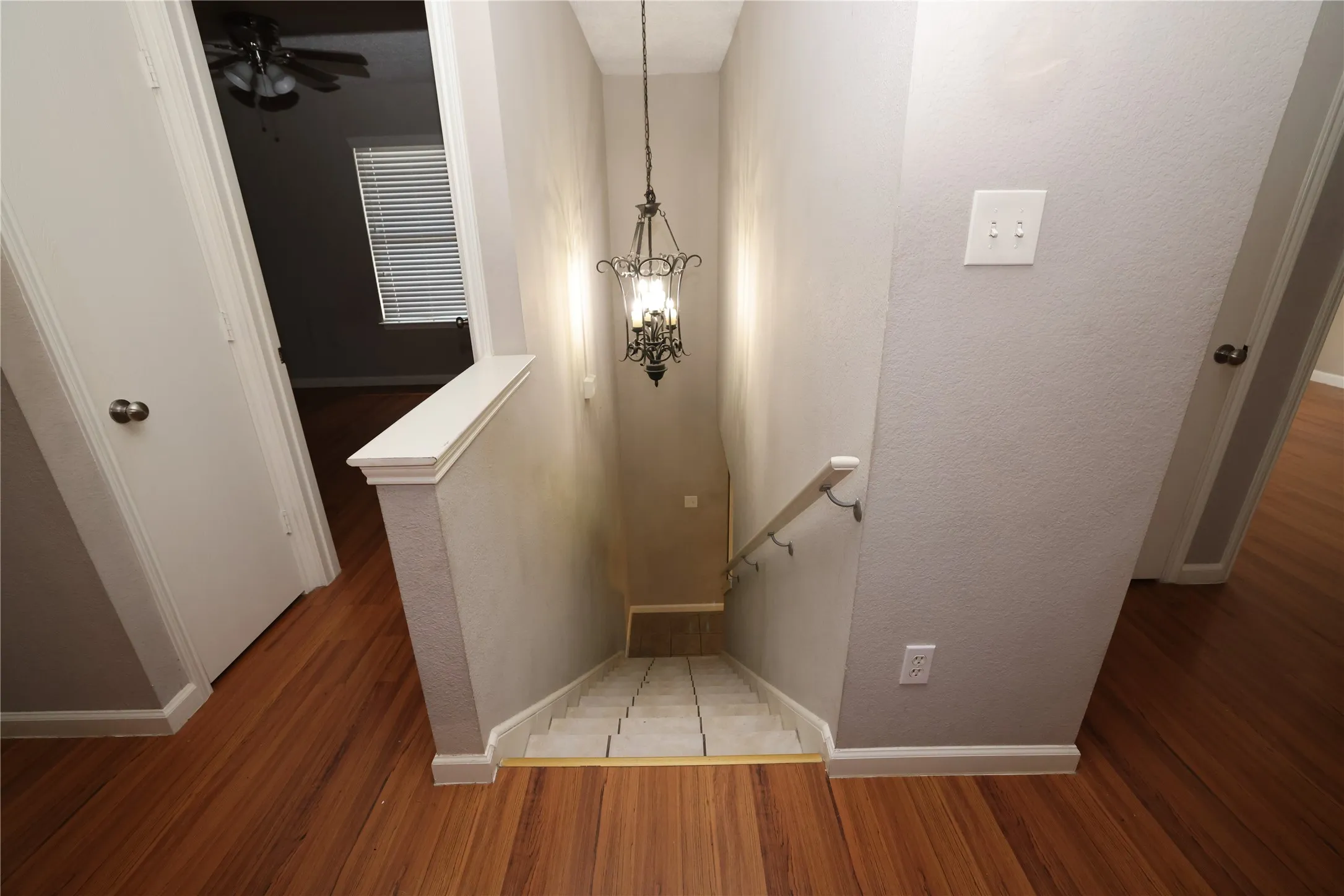Wood-finish flooring throughout, decorative chandelier, wall-mounted light fixture, and staircase with handrail