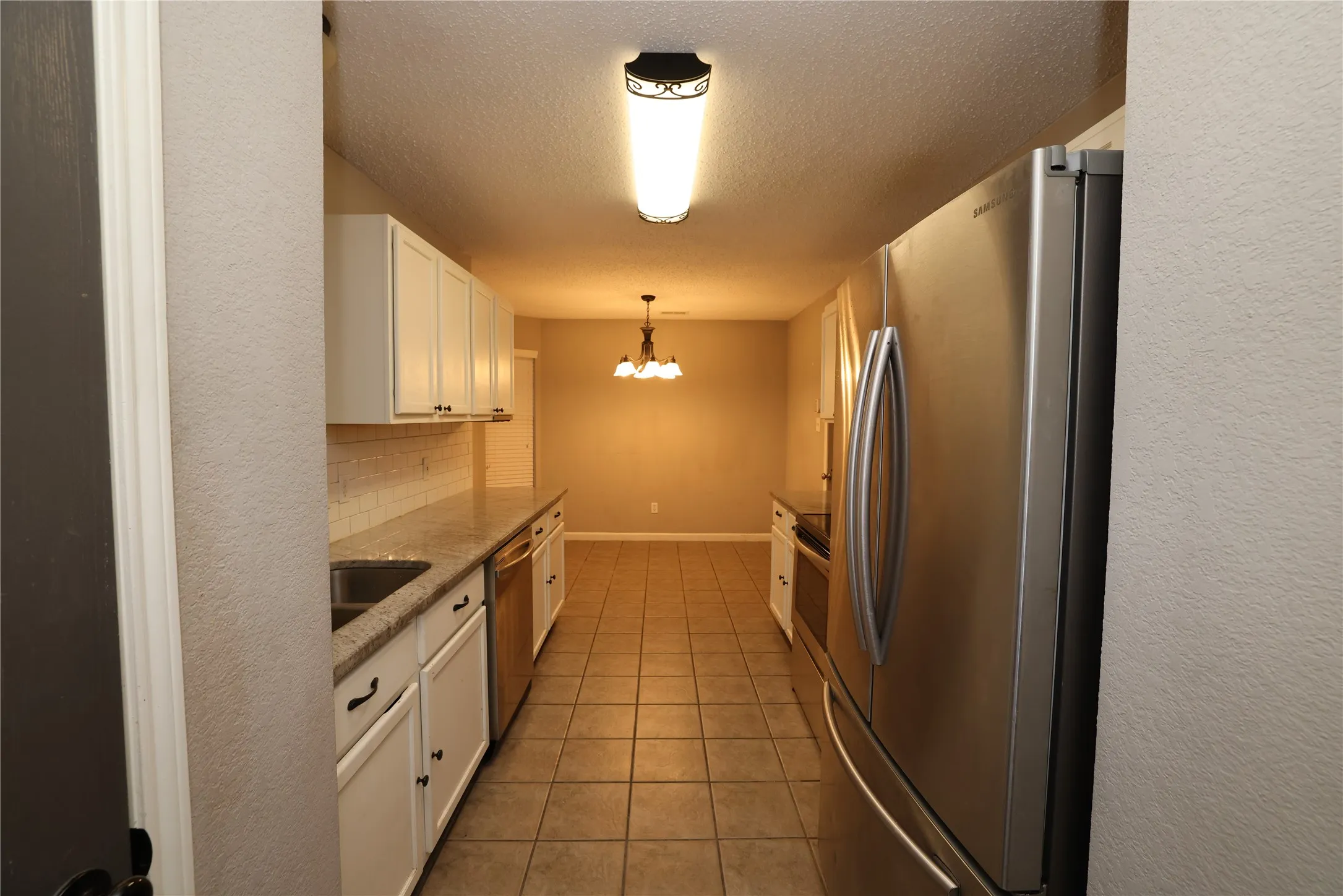 Galley kitchen featuring white cabinetry, stone-finish countertops, stainless steel appliances, and tile flooring