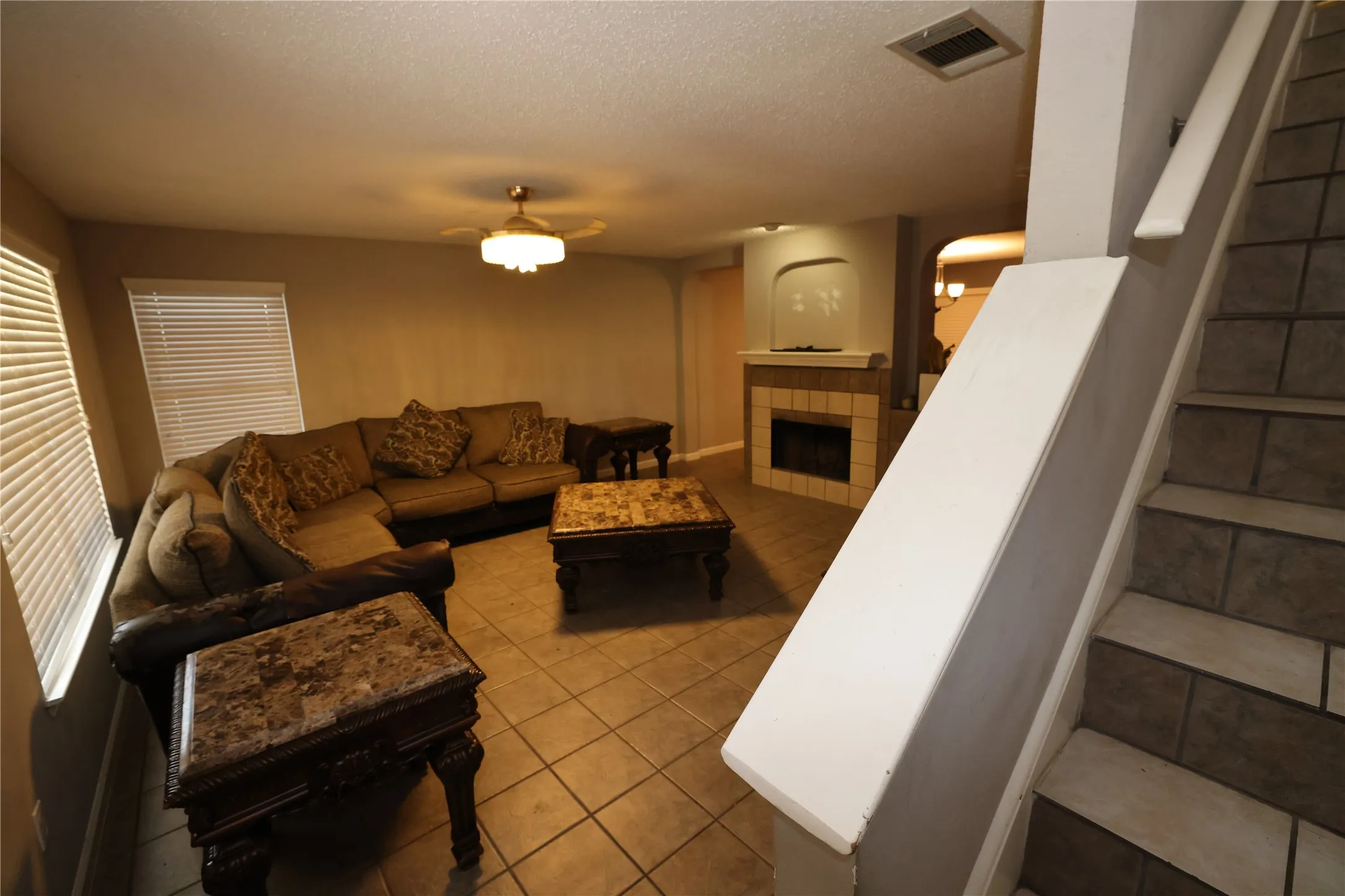 Tile flooring throughout, recessed fireplace, ceiling fan with integrated lighting, window blinds, and tile-front steps