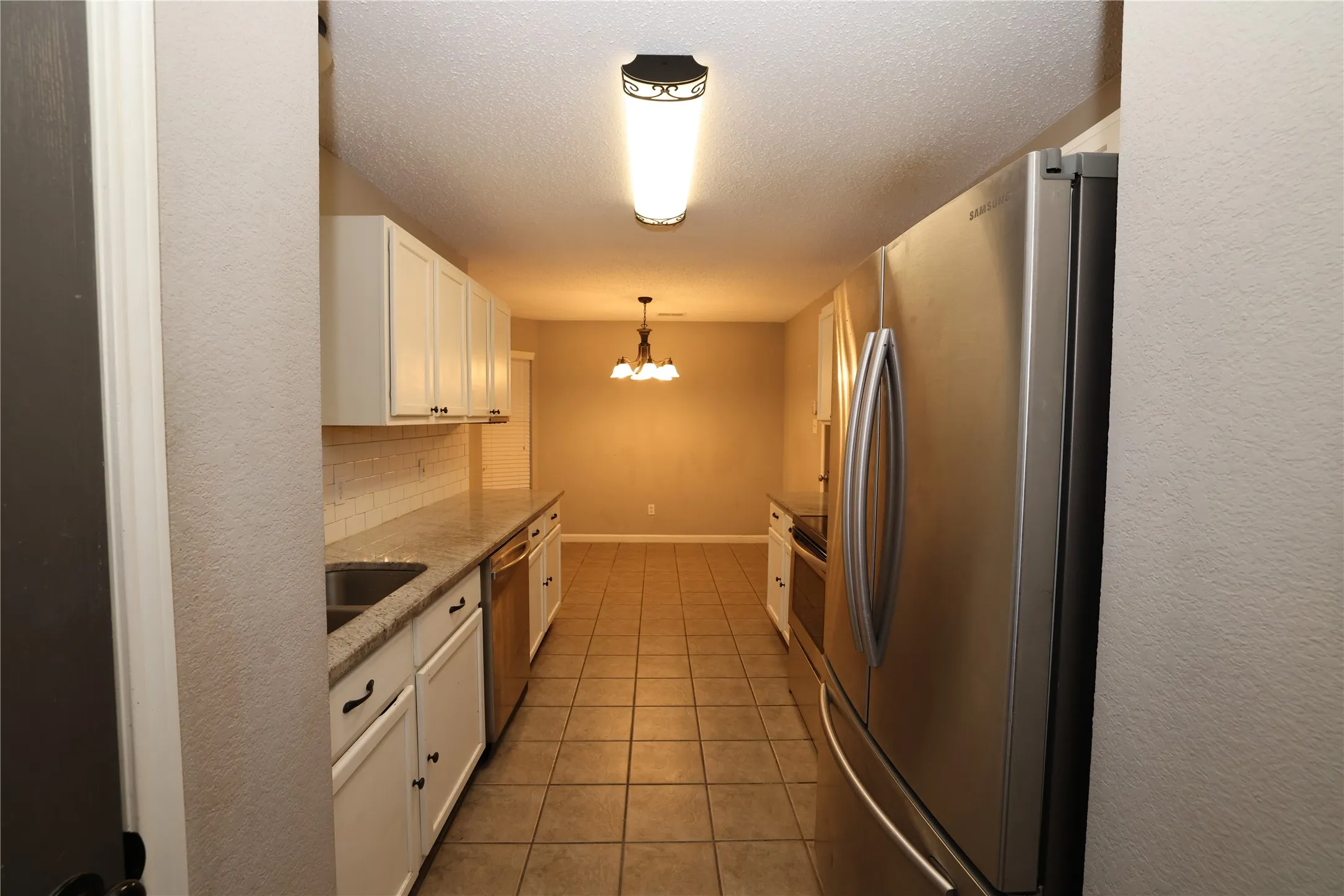 Galley kitchen featuring white cabinetry, granite-style countertops, stainless steel appliances, and a tiled backsplash
