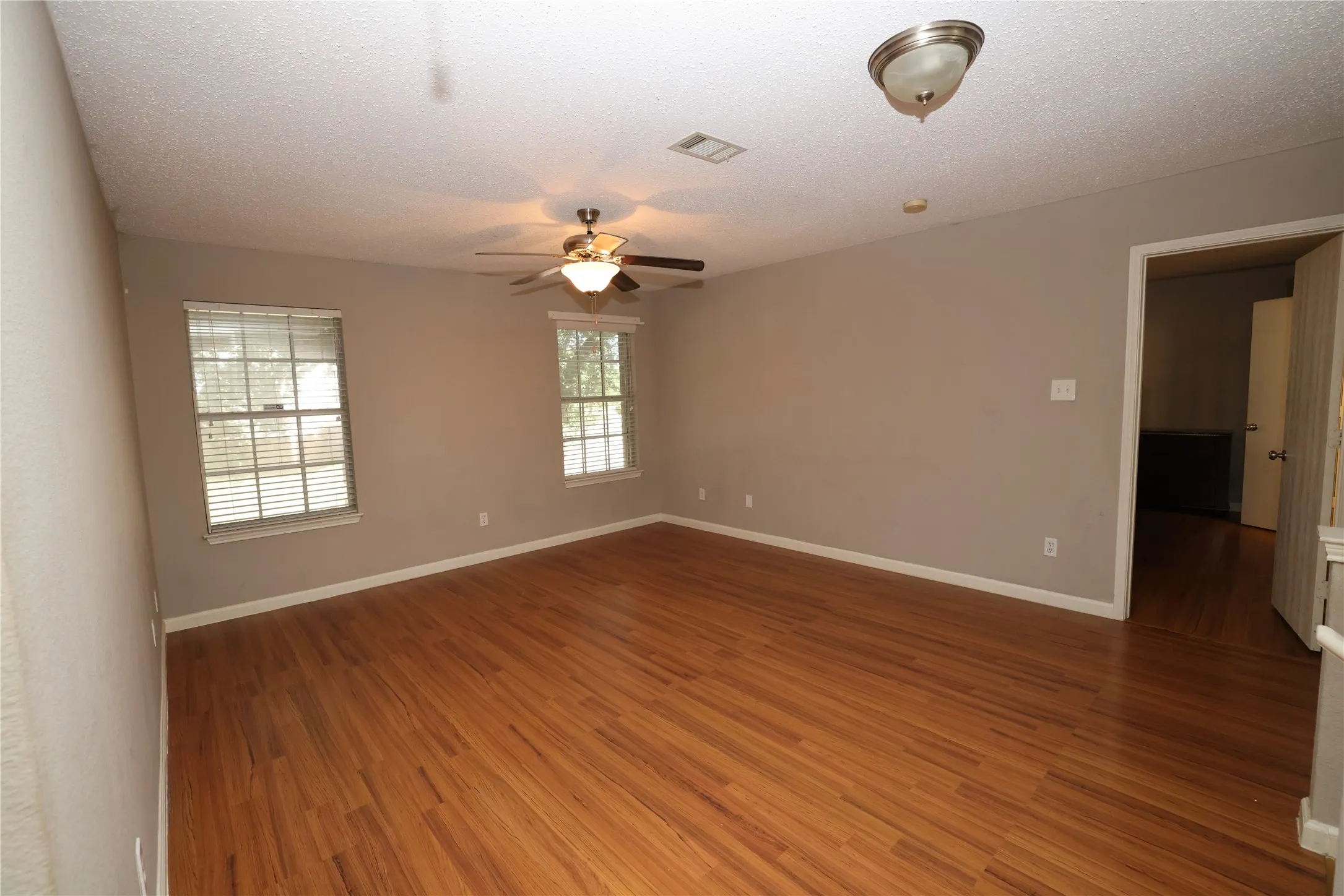 Wood-finish flooring, two windows with blinds, ceiling fan with integrated lighting, and a flush-mount ceiling light