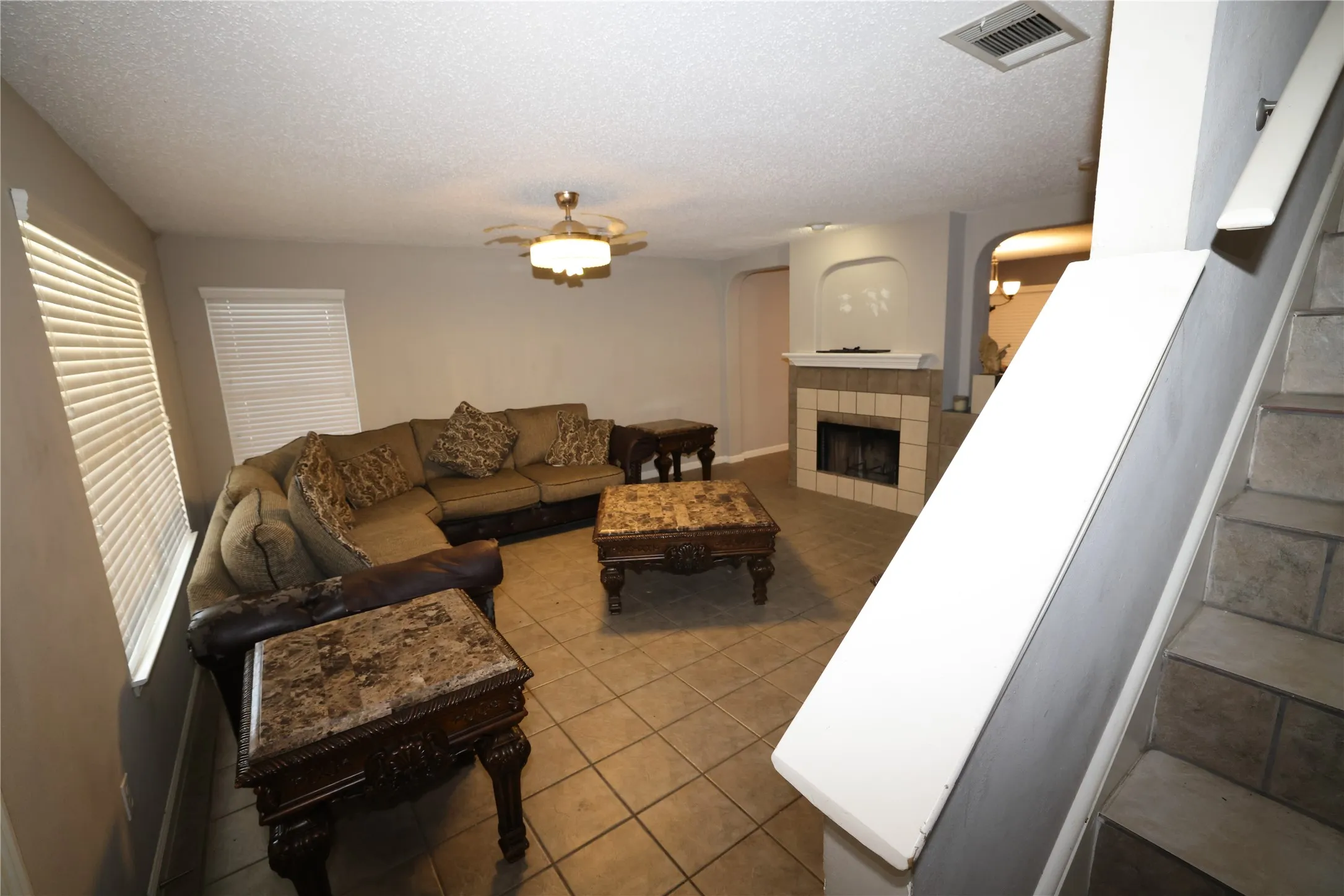 Tile flooring throughout, fireplace with a tiled surround, built-in archway details, and a ceiling fan with integrated lighting