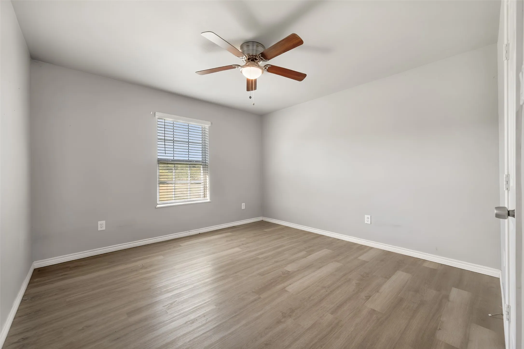 Bright and spacious bedroom featuring hardwood flooring, a ceiling fan with integrated lighting, large window with plantation shutters, and fresh neutral wall finishes throughout