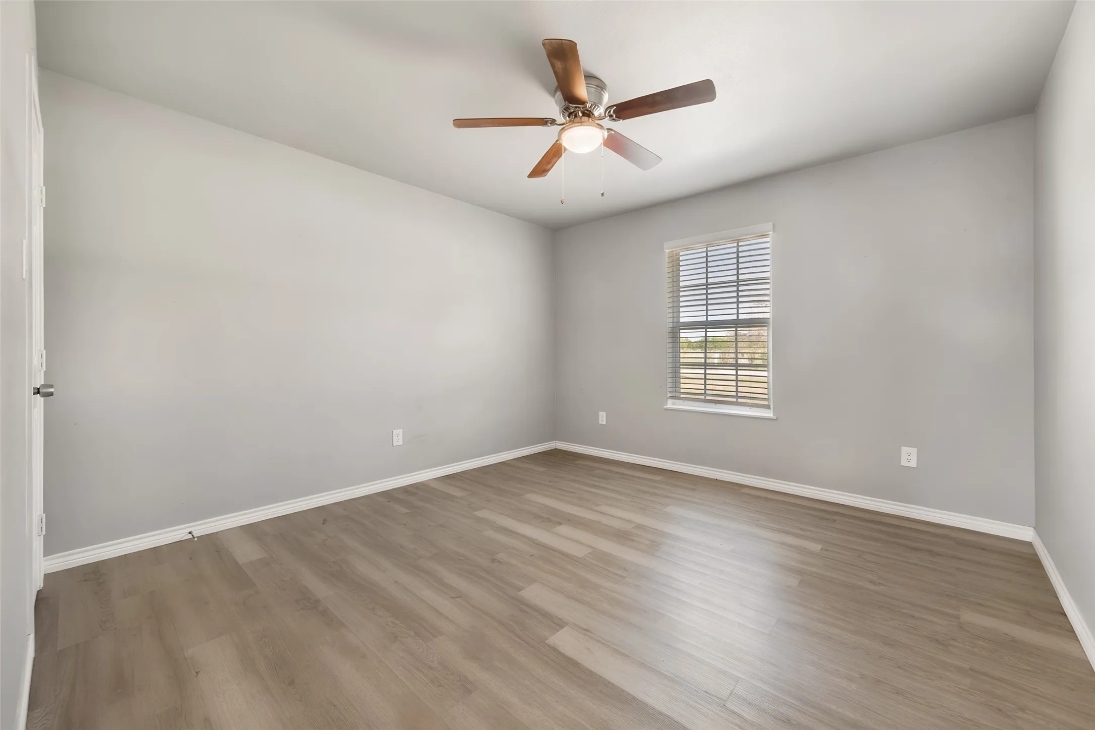 Wood-finish flooring, single window with blinds, ceiling fan with light fixture, and neutral wall paint