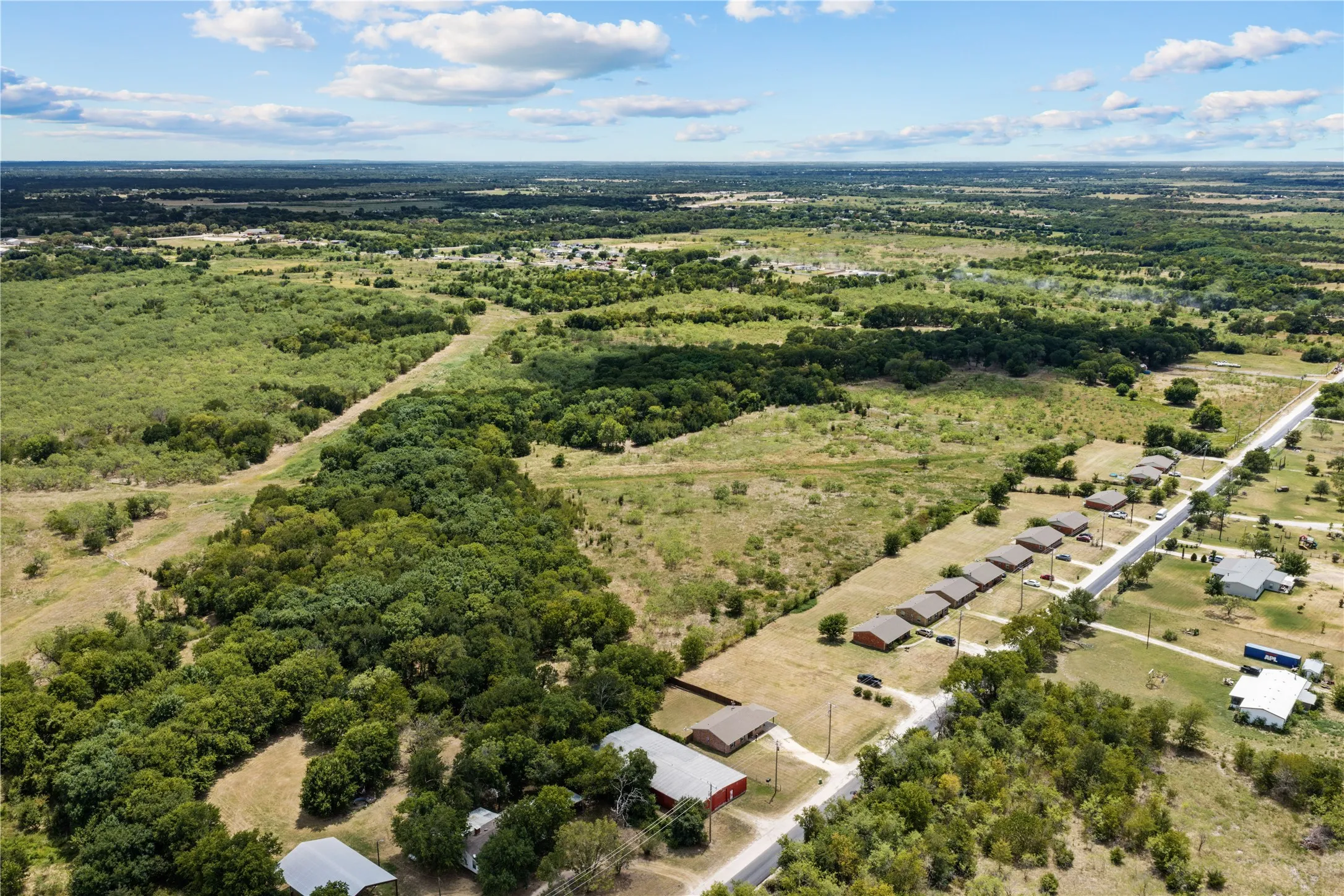 Expansive rural landscape featuring scattered residential properties, mature tree lines, and open fields under a clear sky