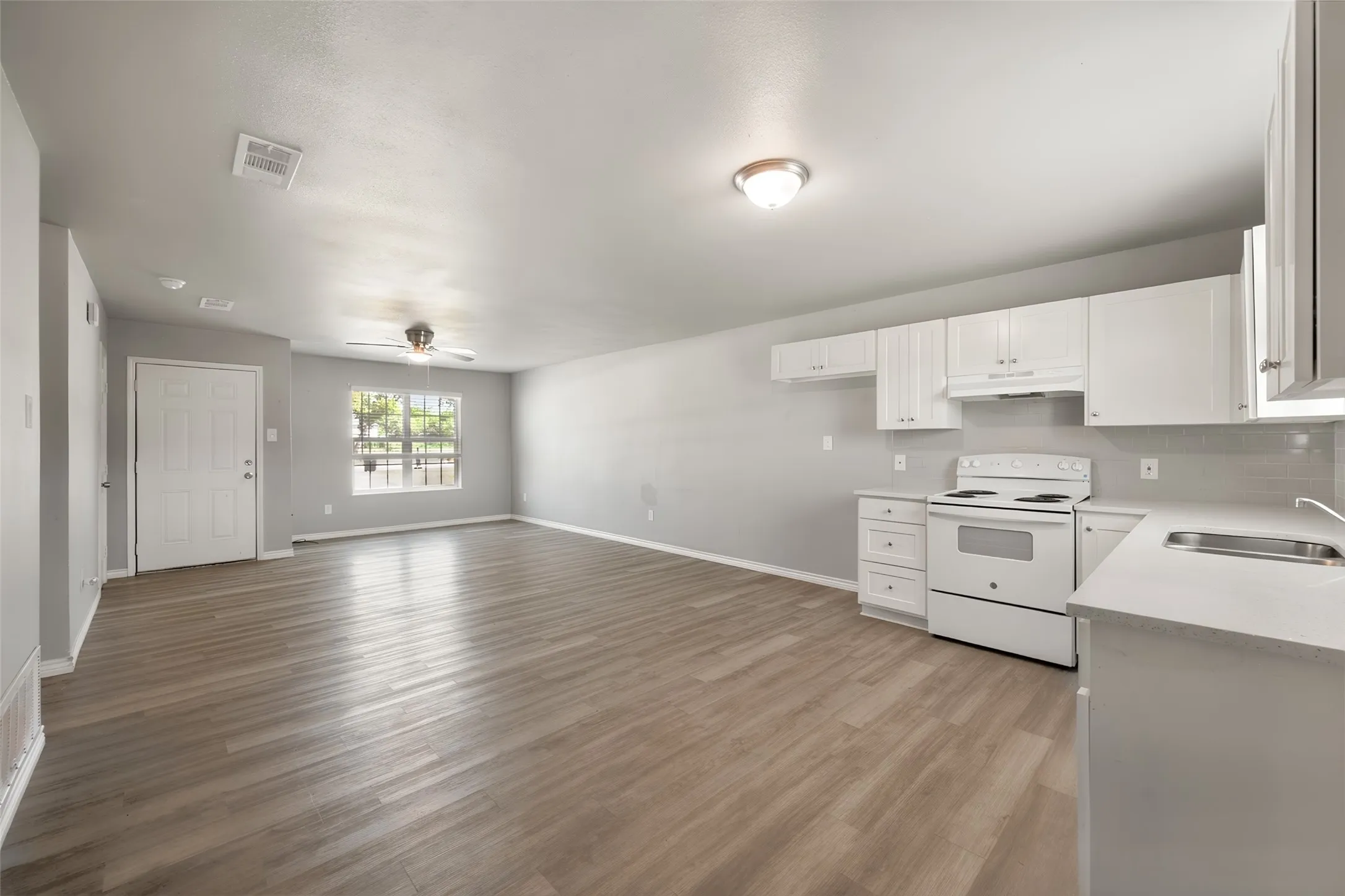 Open concept living space with wood-finish flooring, white cabinetry, integrated stainless steel sink, and a white electric range