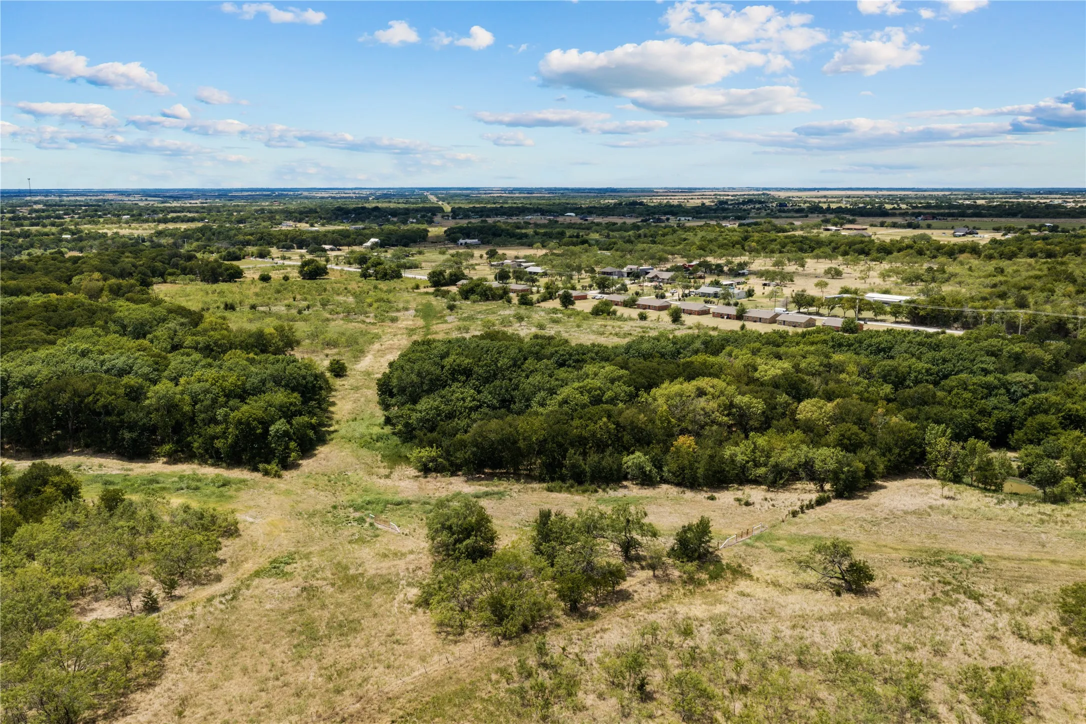 Expansive acreage featuring mature trees and open fields under a clear sky