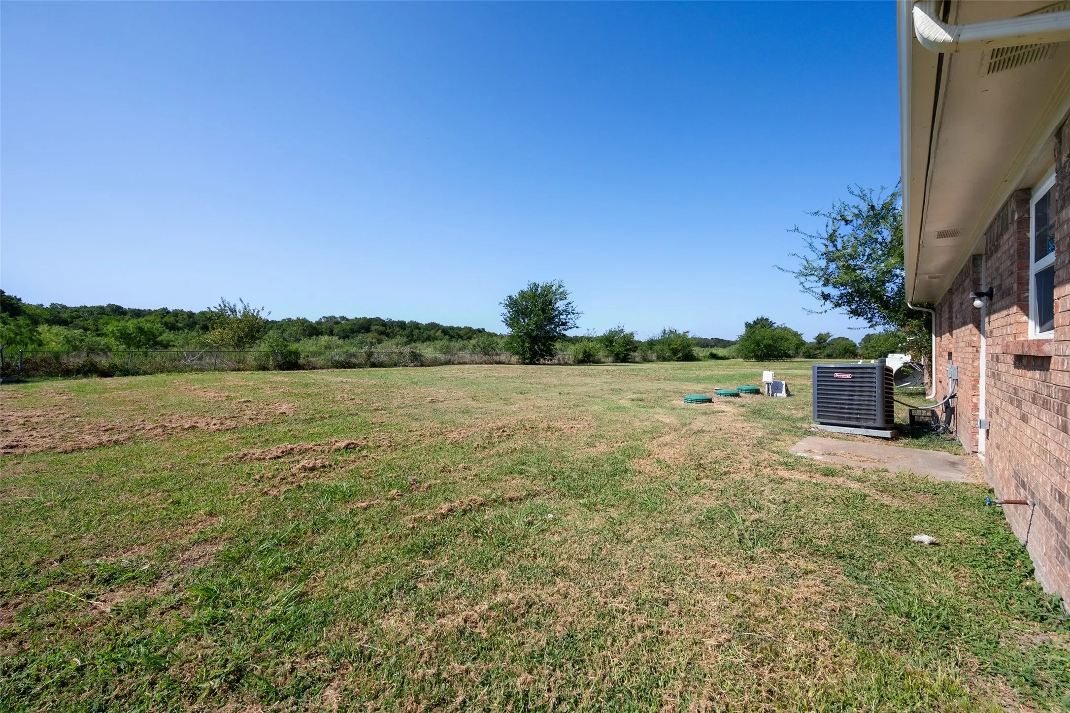 Expansive grassy area featuring a visible air conditioning unit and brick exterior