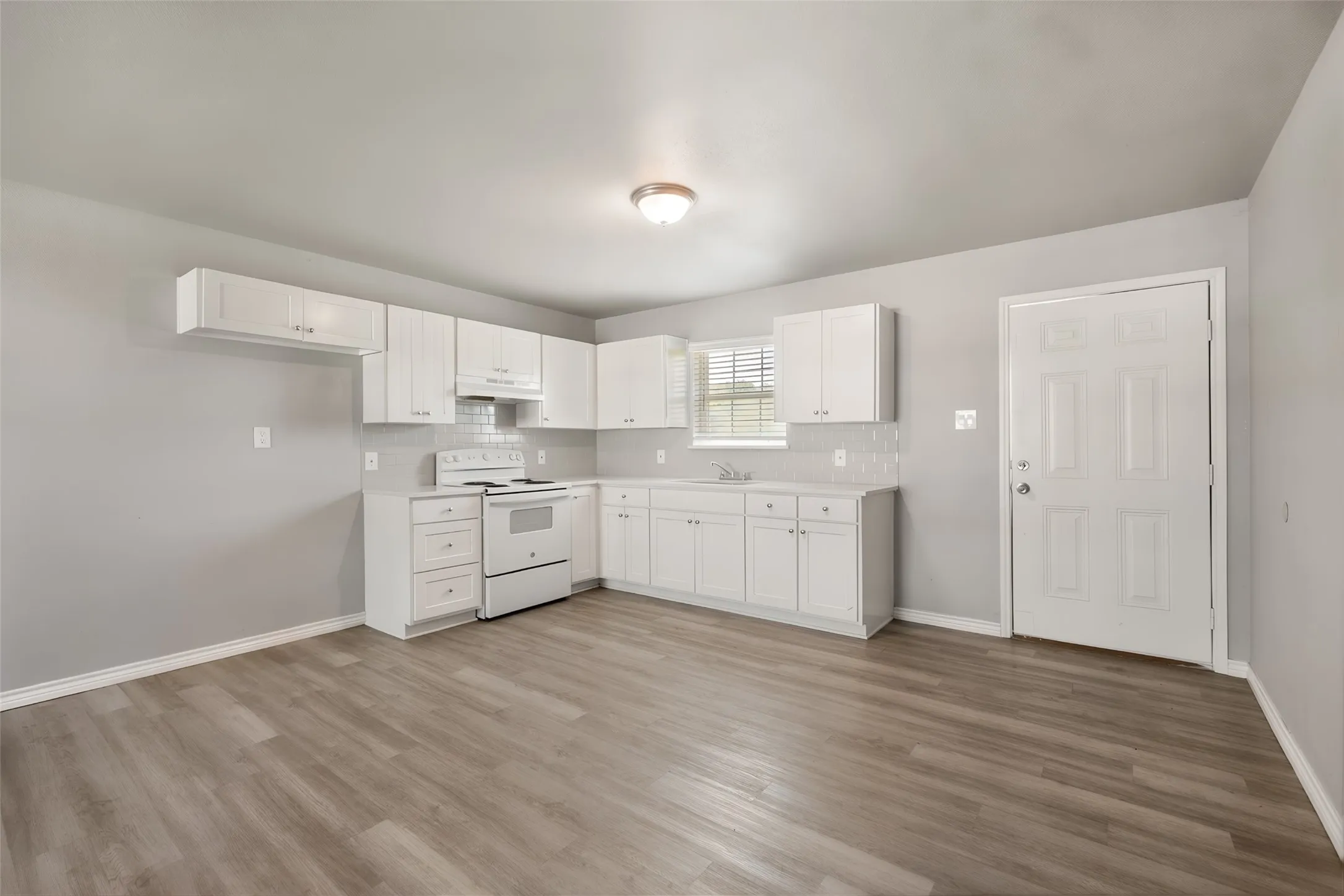 Wood-finish flooring, white cabinetry, light gray walls, white appliance package, and a tile backsplash