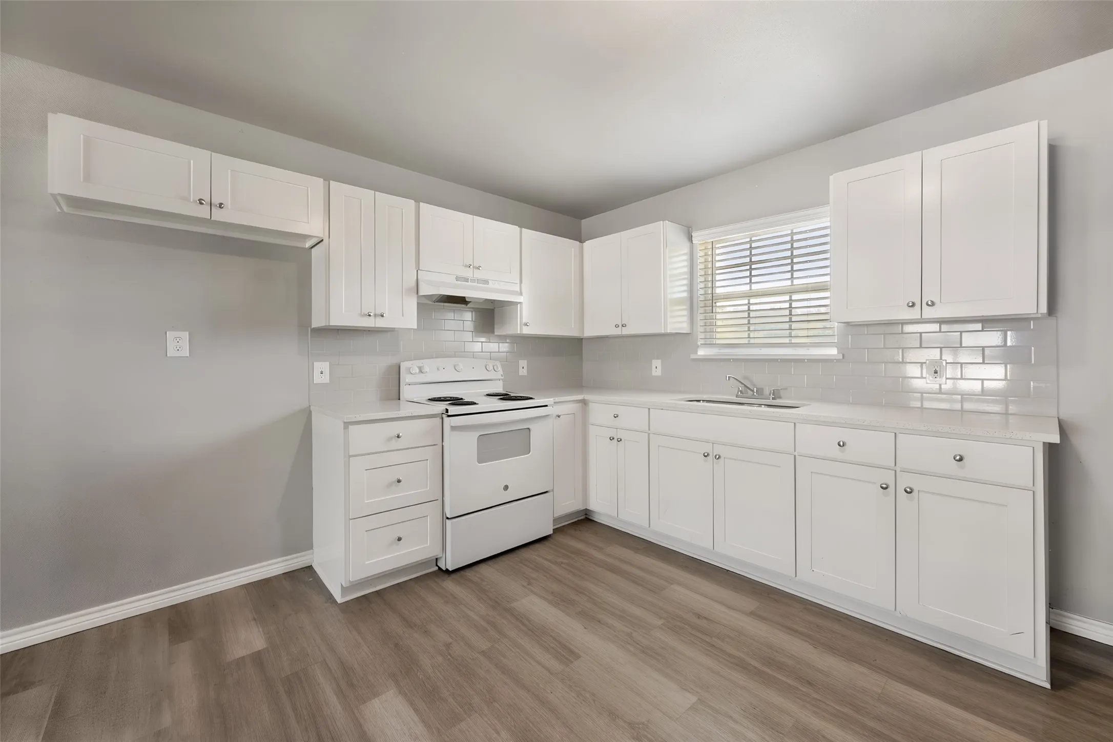 Kitchen featuring white shaker-style cabinetry, light-toned countertops, subway tile backsplash, and wood-finish flooring