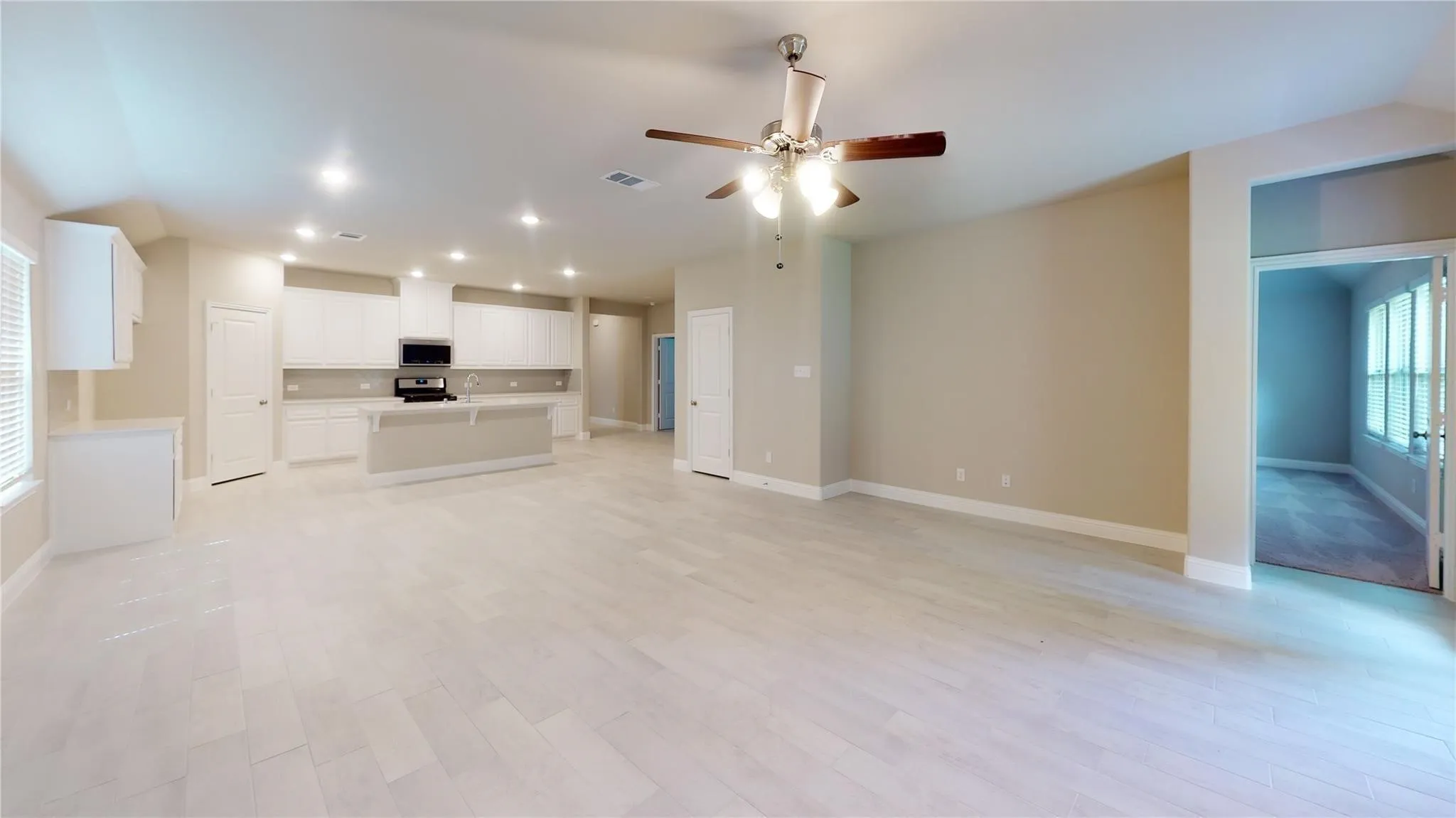 Open-concept living area featuring light wood-finish flooring, a contemporary ceiling fan, recessed lighting, and a kitchen with white cabinetry and a central island